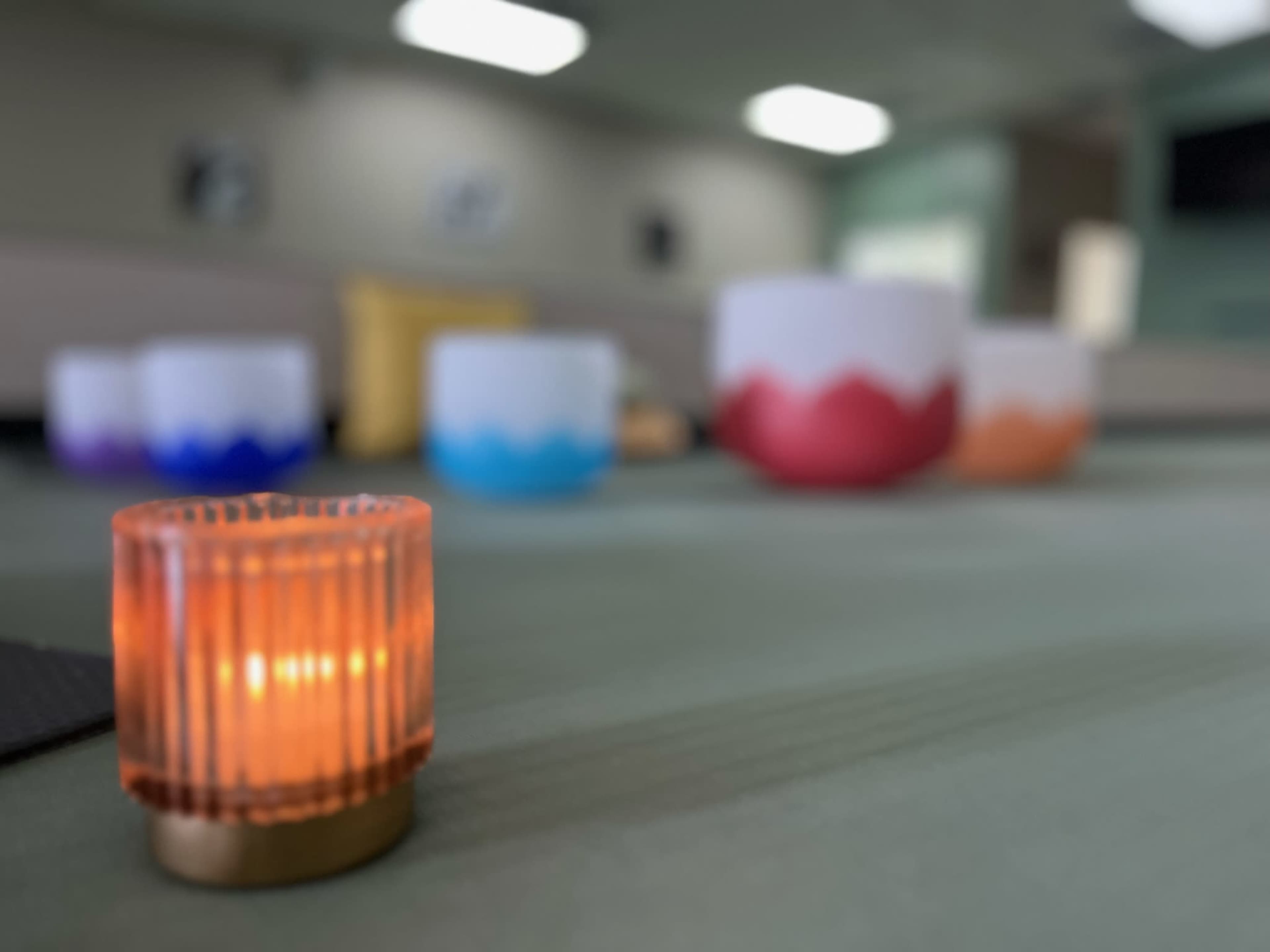 A small orange candle sits in the foreground with various colored bowls out of focus in the background.