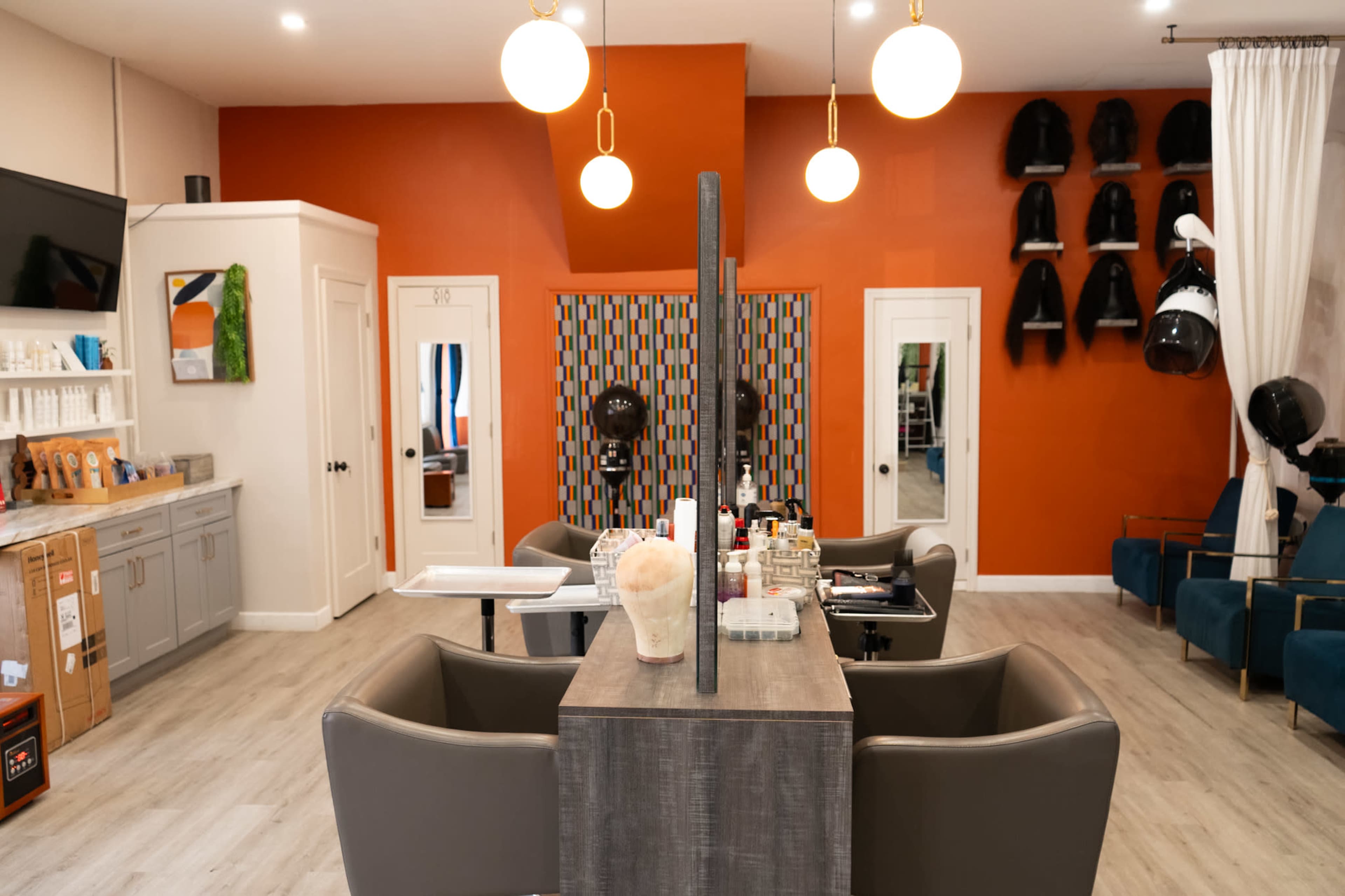 The image shows a modern salon interior featuring multiple styling chairs, a divided work area, and hairdryers mounted on the wall.