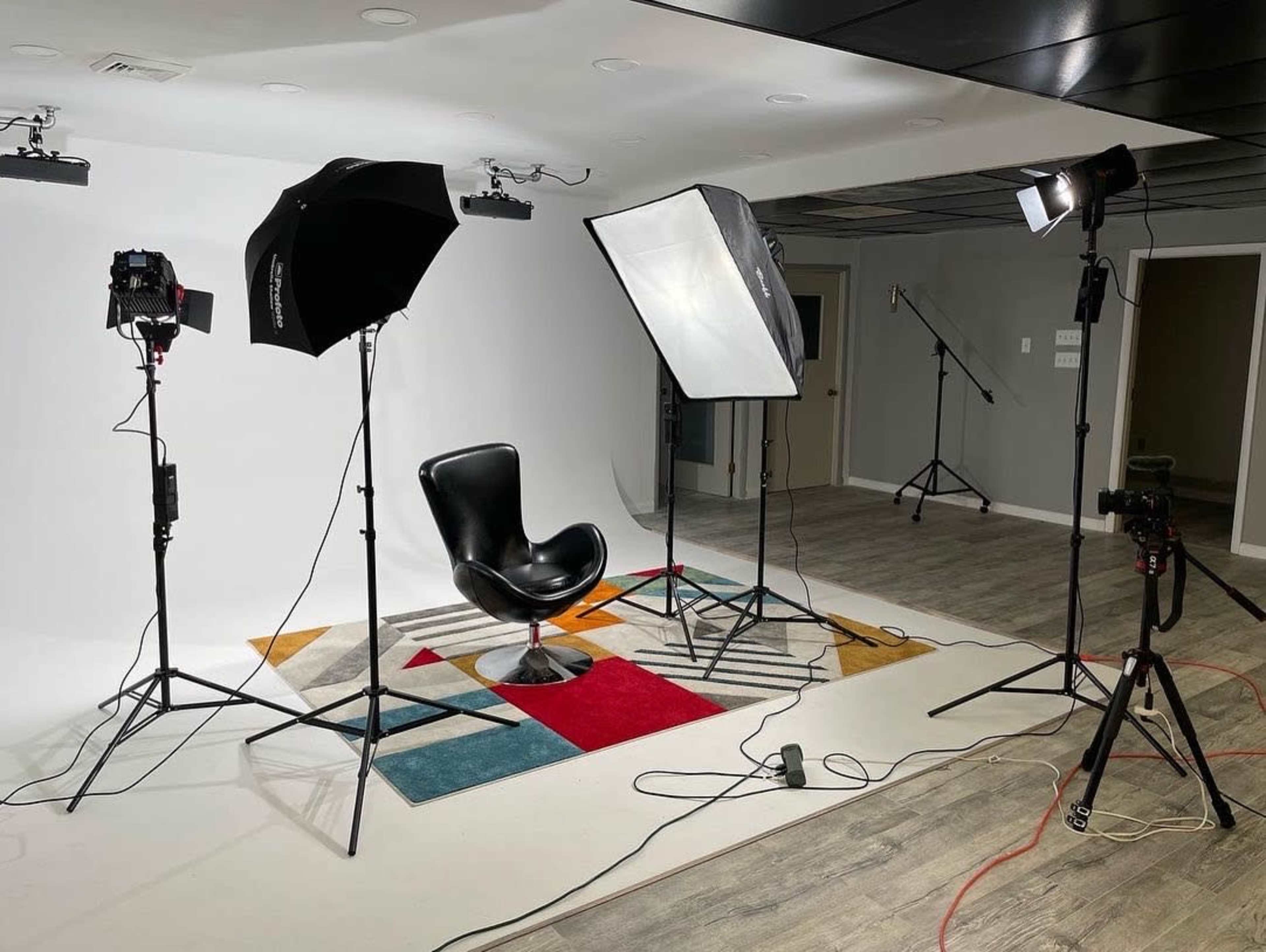 A photography studio setup with a black chair on a colorful rug, surrounded by studio lights and camera equipment.