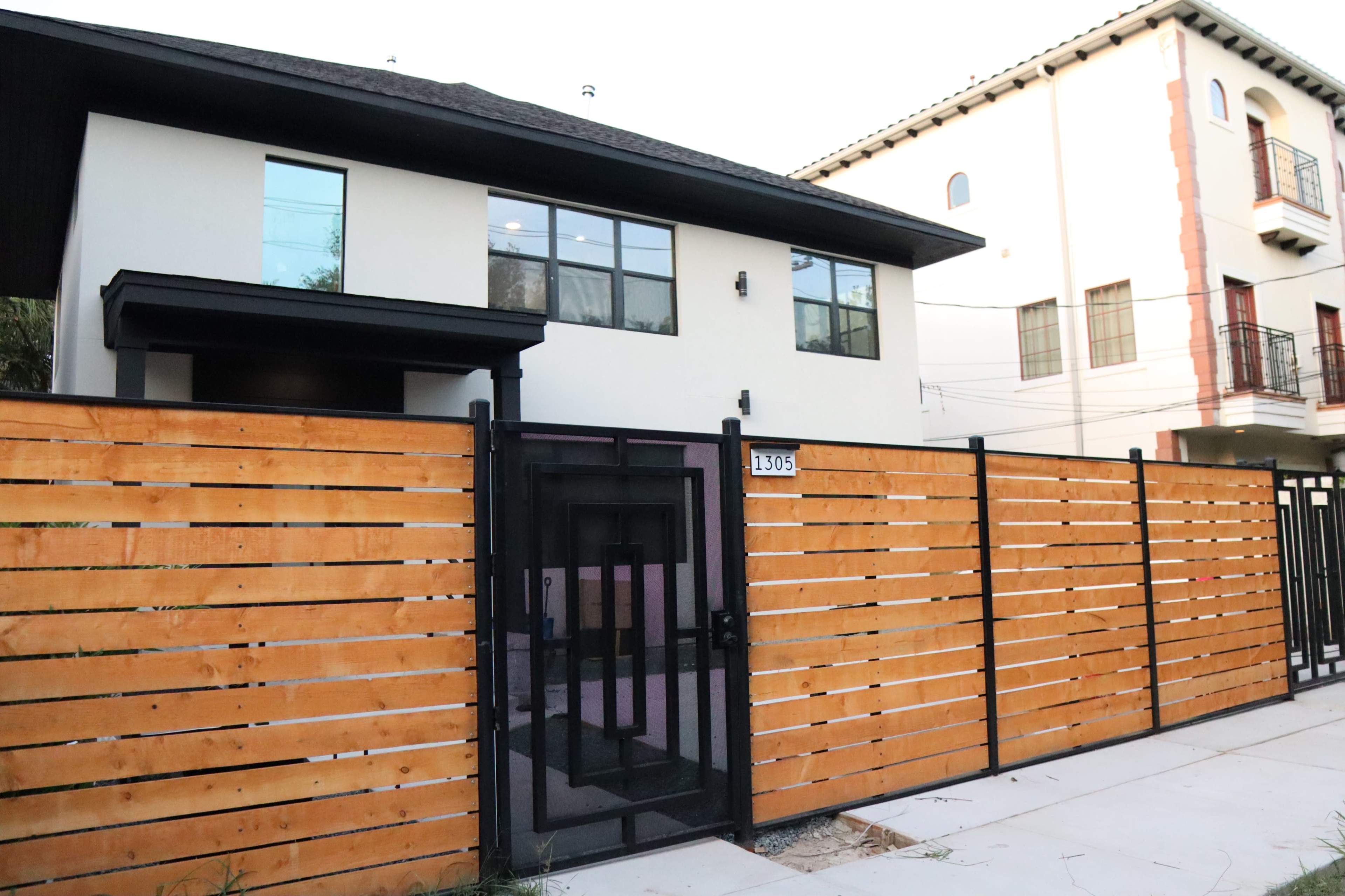 A modern two-story house with large windows and a wooden fence surrounding the front property.