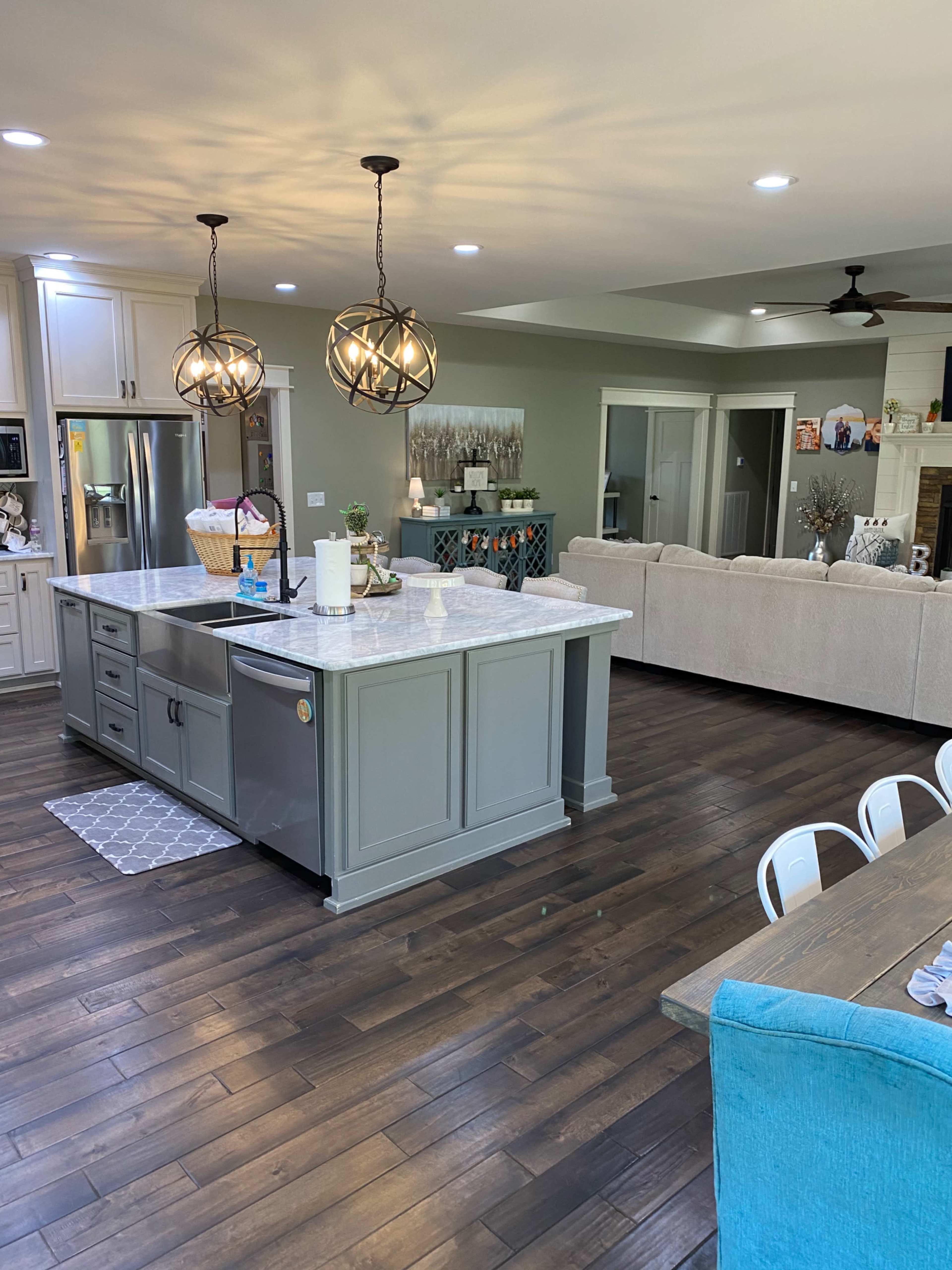 A modern kitchen with an island, pendant lights, and a living area with a sofa and dining table.