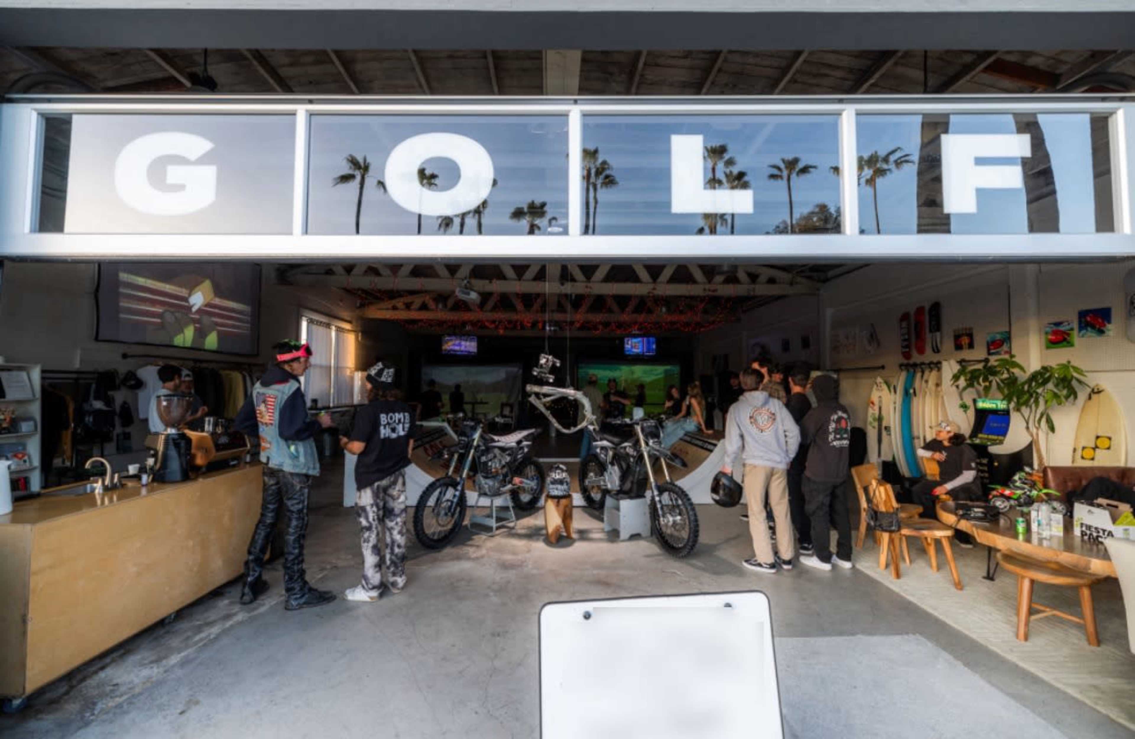 The scene shows a trendy retail space with large "GOLF" signage, featuring customers browsing and socializing, along with a motorcycle and surfboards on display.
