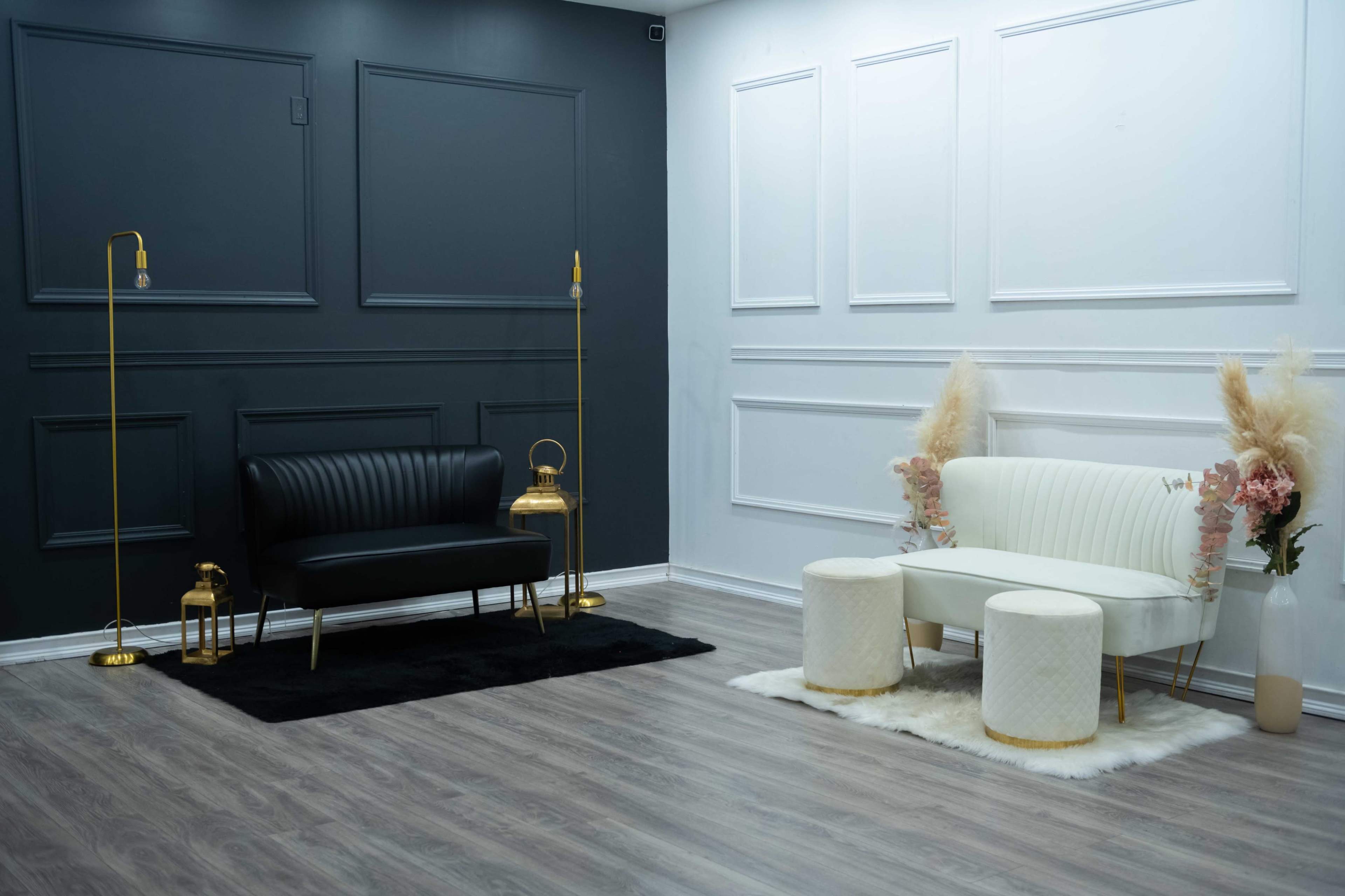 The image shows a modern interior with a black accent wall, a black sofa, a white settee, and two white stools on a wooden floor.