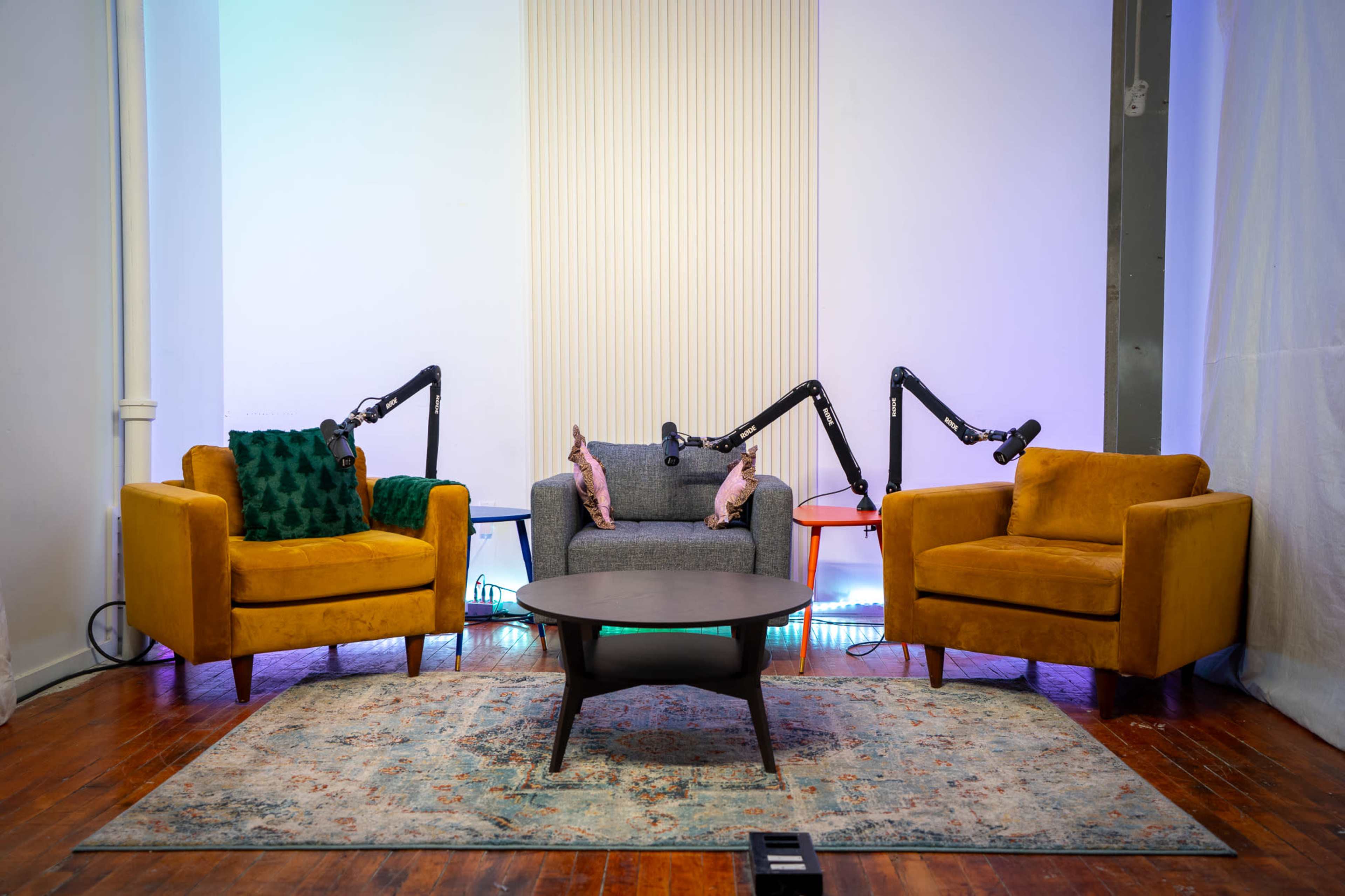 The image depicts a cozy seating arrangement with two mustard-colored armchairs flanking a gray couch, all situated around a round table on a patterned rug in a brightly lit room.