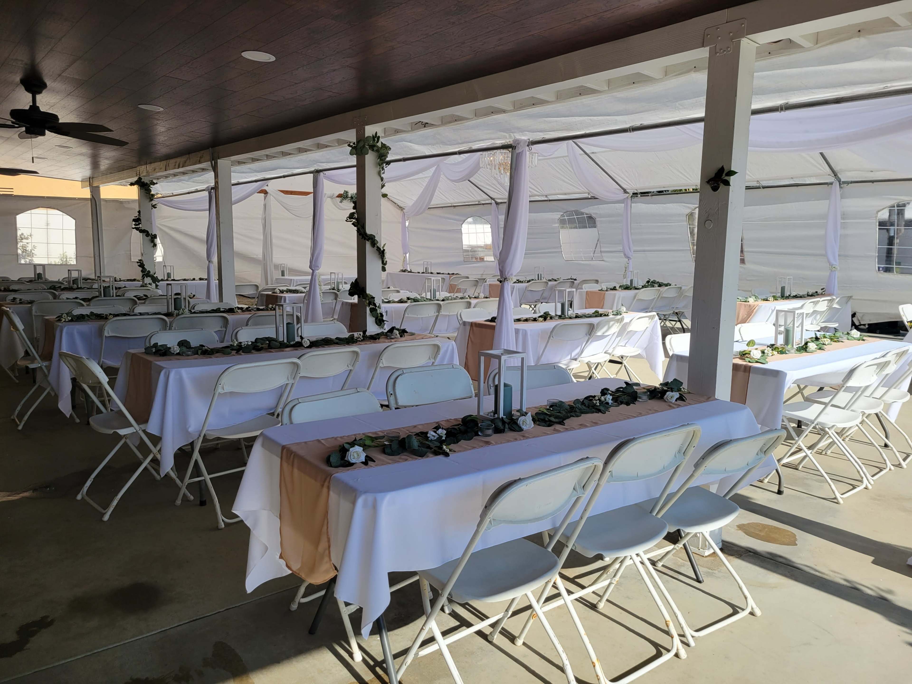 A covered outdoor venue with several rows of tables set with white tablecloths and decorated with greenery.