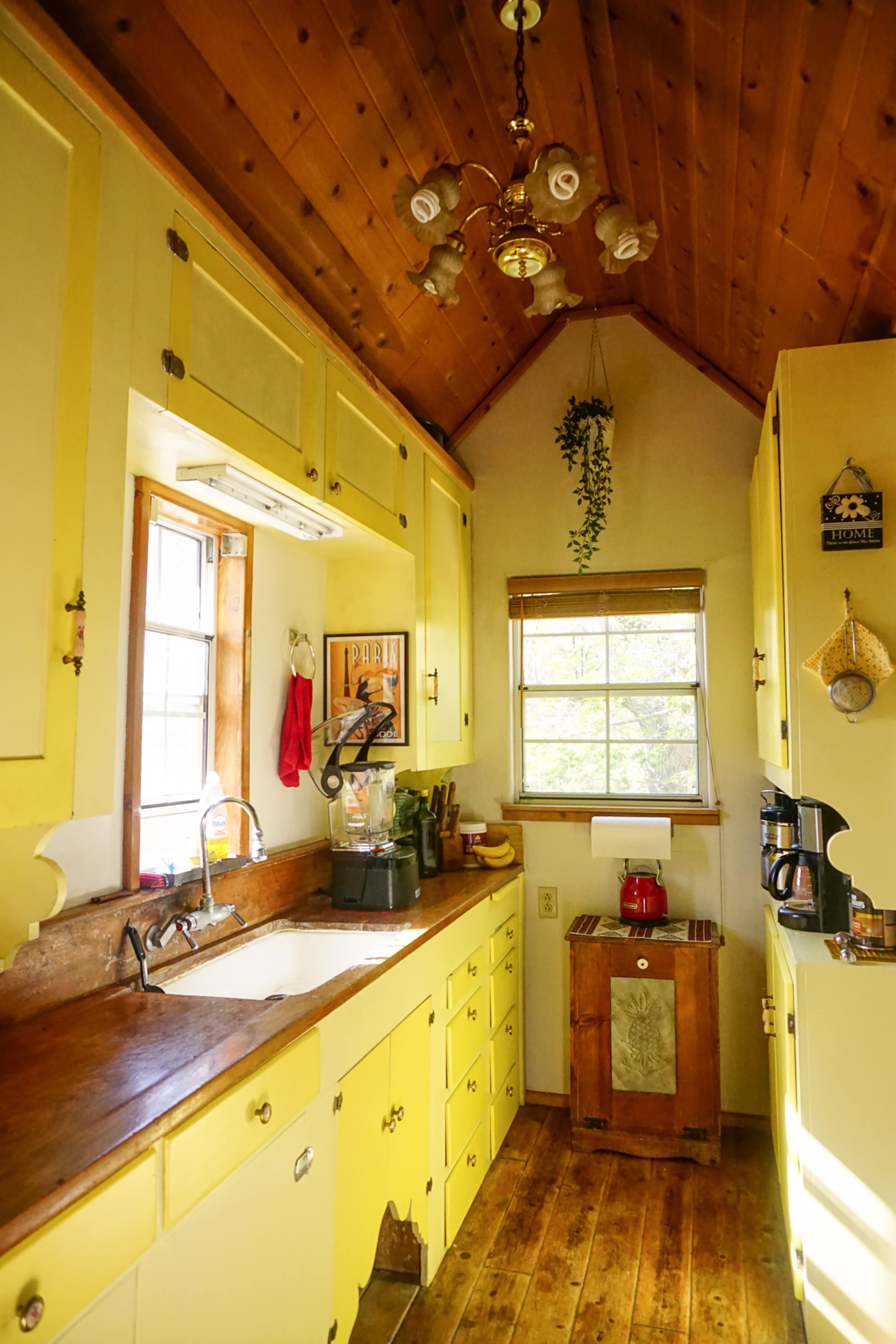A small kitchen with yellow cabinets, wooden countertops, and a sloped ceiling, featuring a sink, coffee maker, and window with natural light.