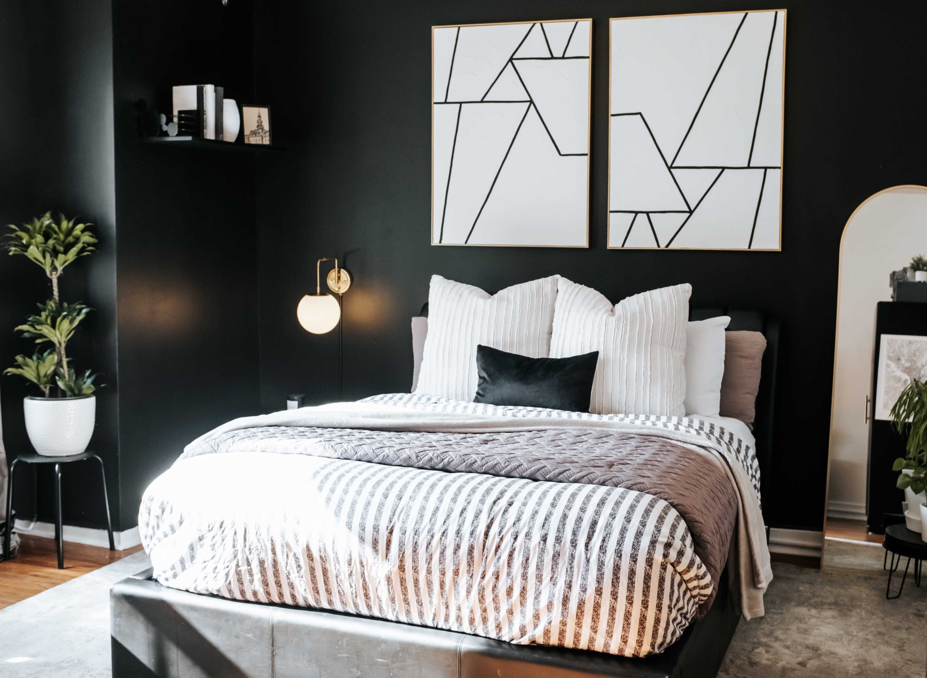 A neatly arranged bedroom features a dark wall, a patterned bedspread, and two framed abstract artworks above the bed.