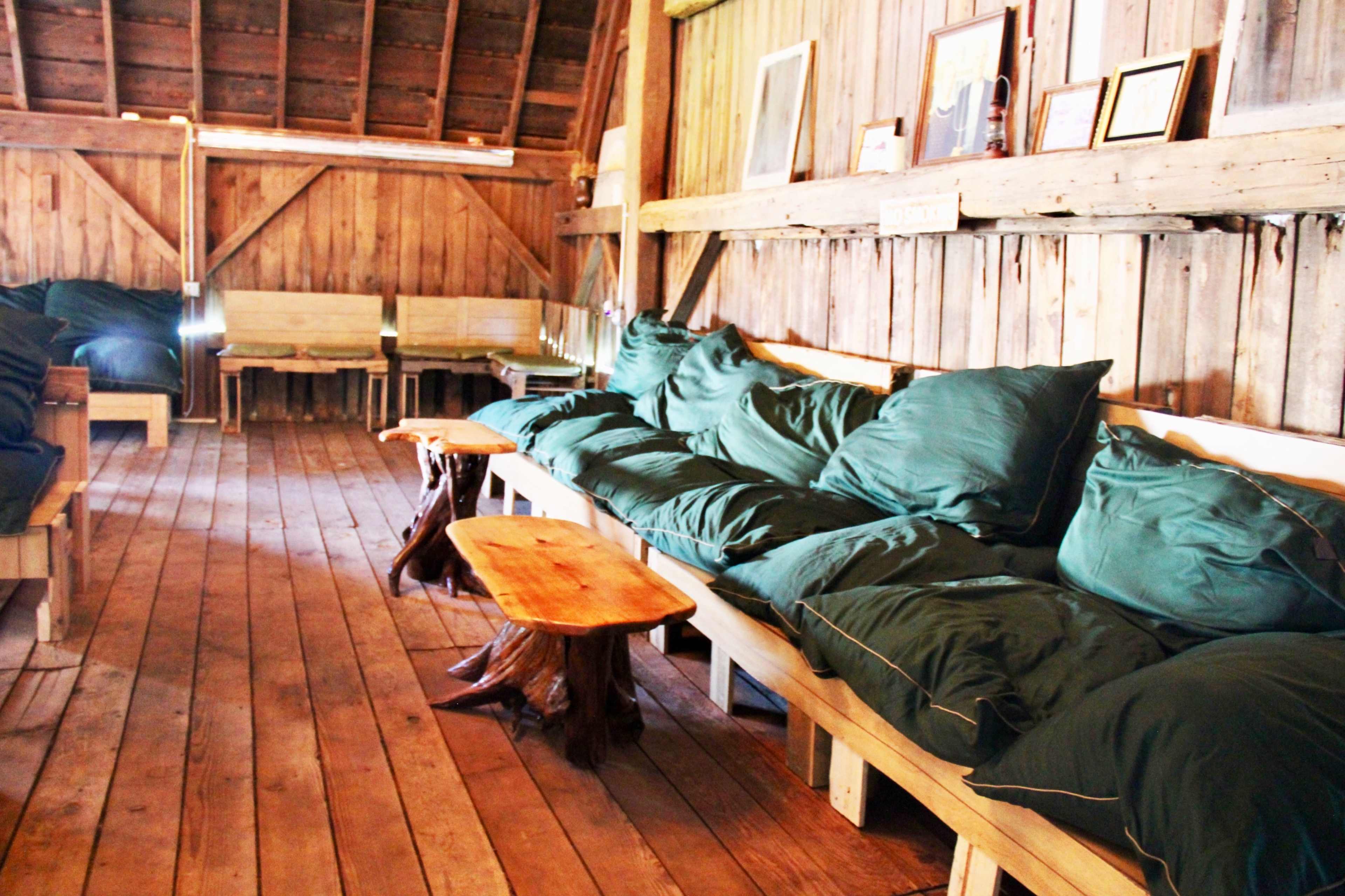 The image shows a cozy wooden interior with benches covered in green cushions and small wooden tables.