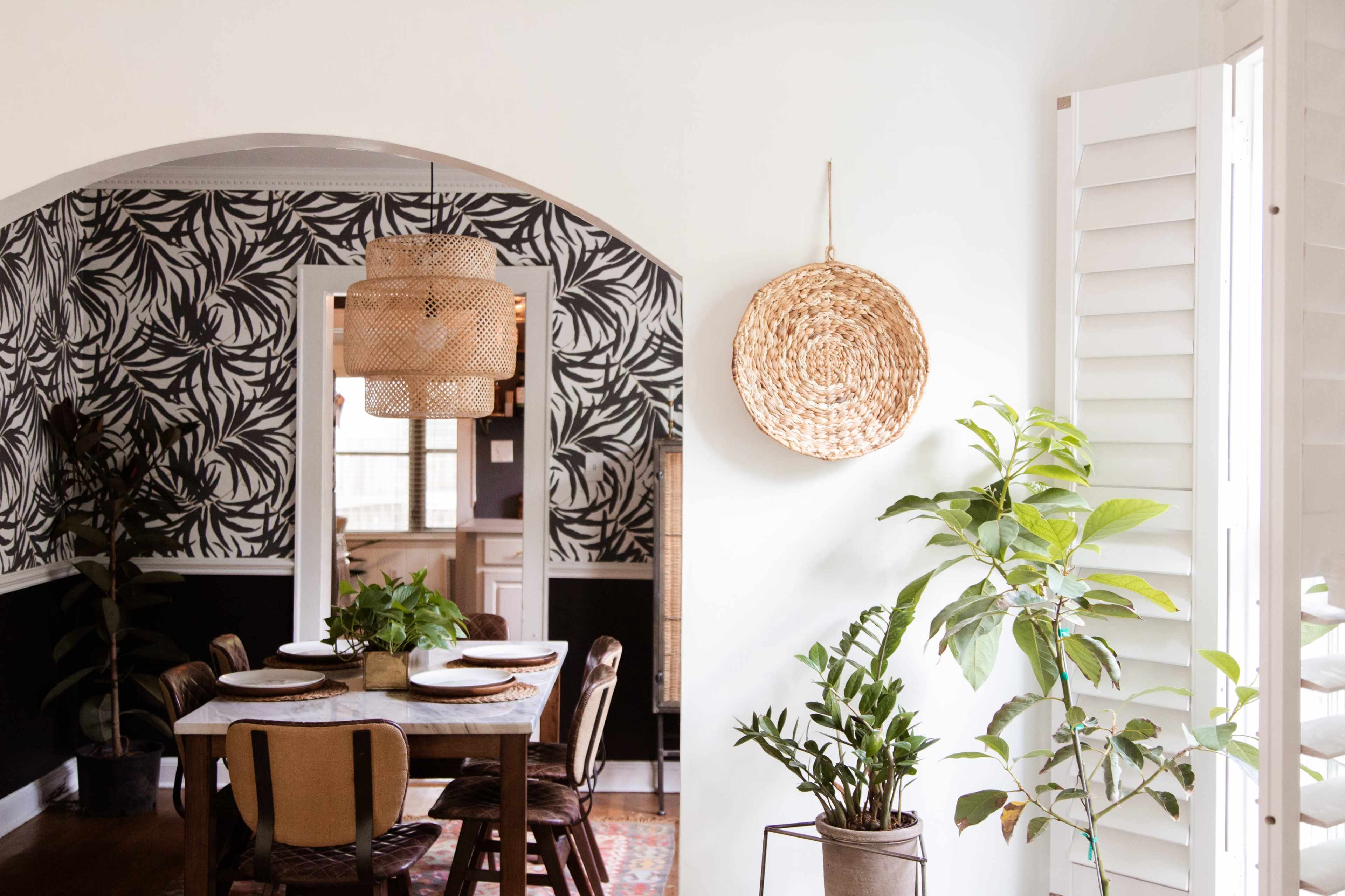 A dining area featuring a wooden table set for meals, surrounded by chairs, with a patterned wallpaper and decorative baskets on the walls.