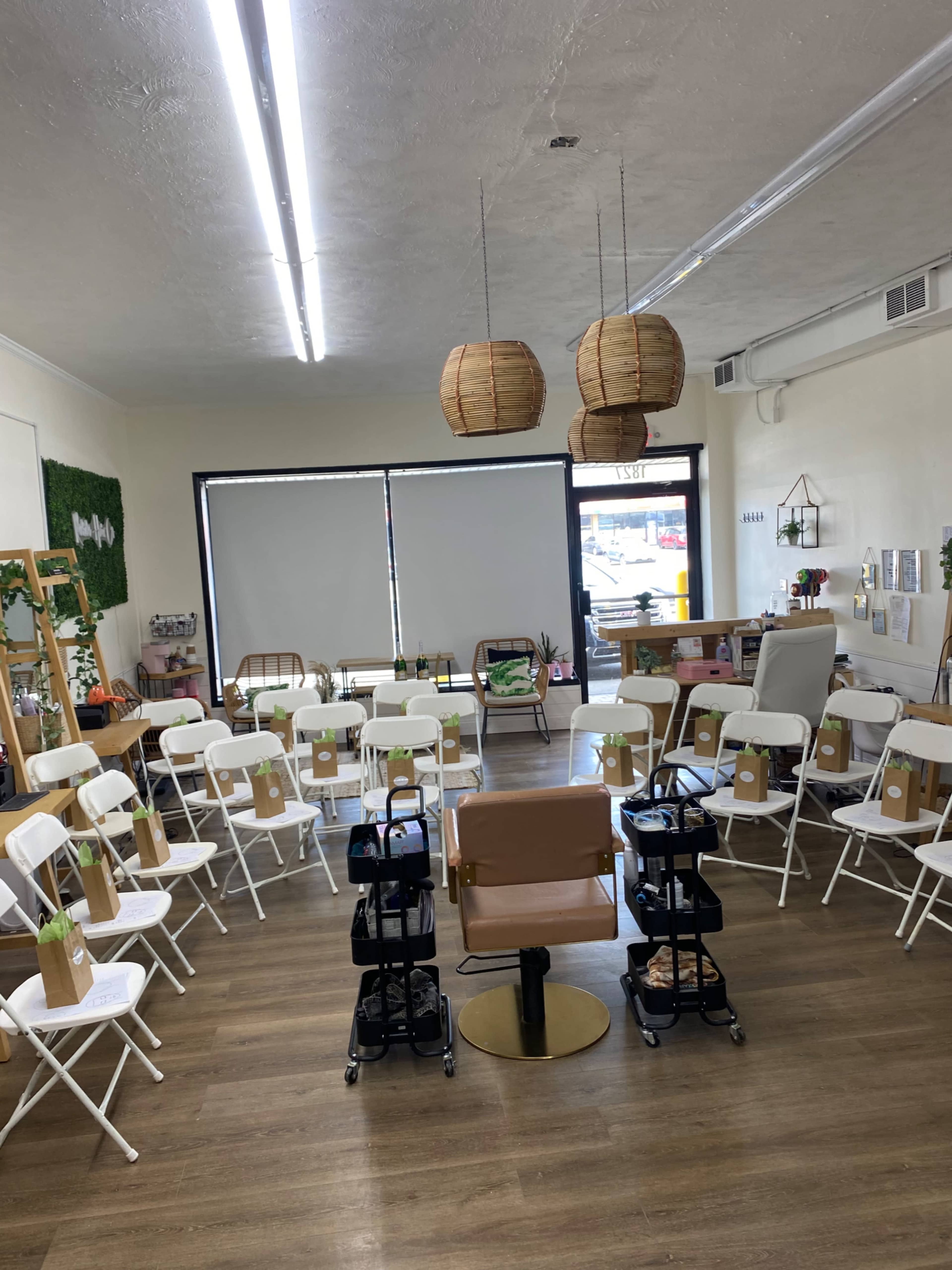 A brightly lit room is set up with white chairs arranged in a circle around a central seat, with hanging lanterns above and a decorative green wall in the background.