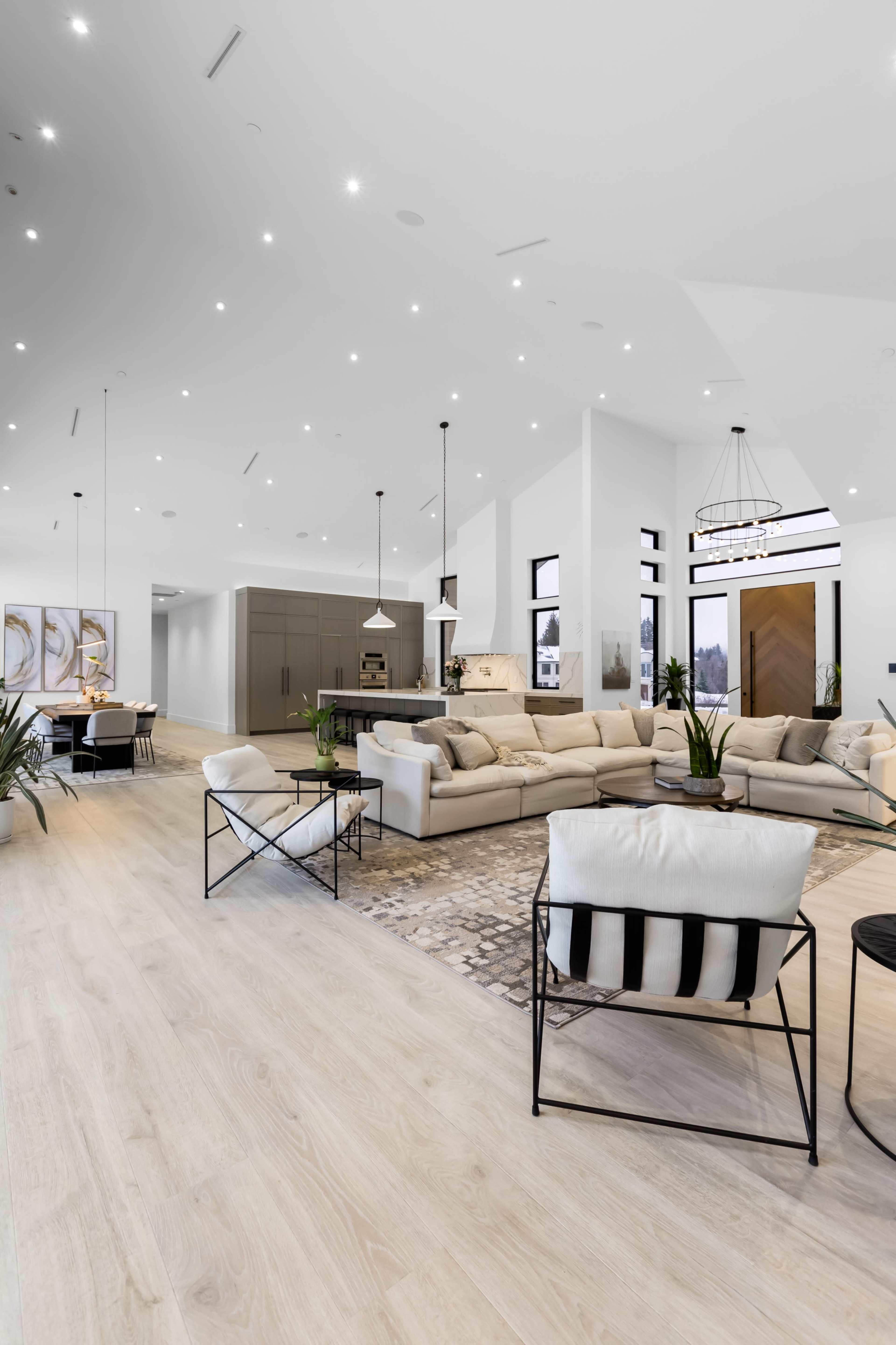 The spacious living area features a light-colored sofa, modern furniture, and large windows allowing natural light to fill the room.