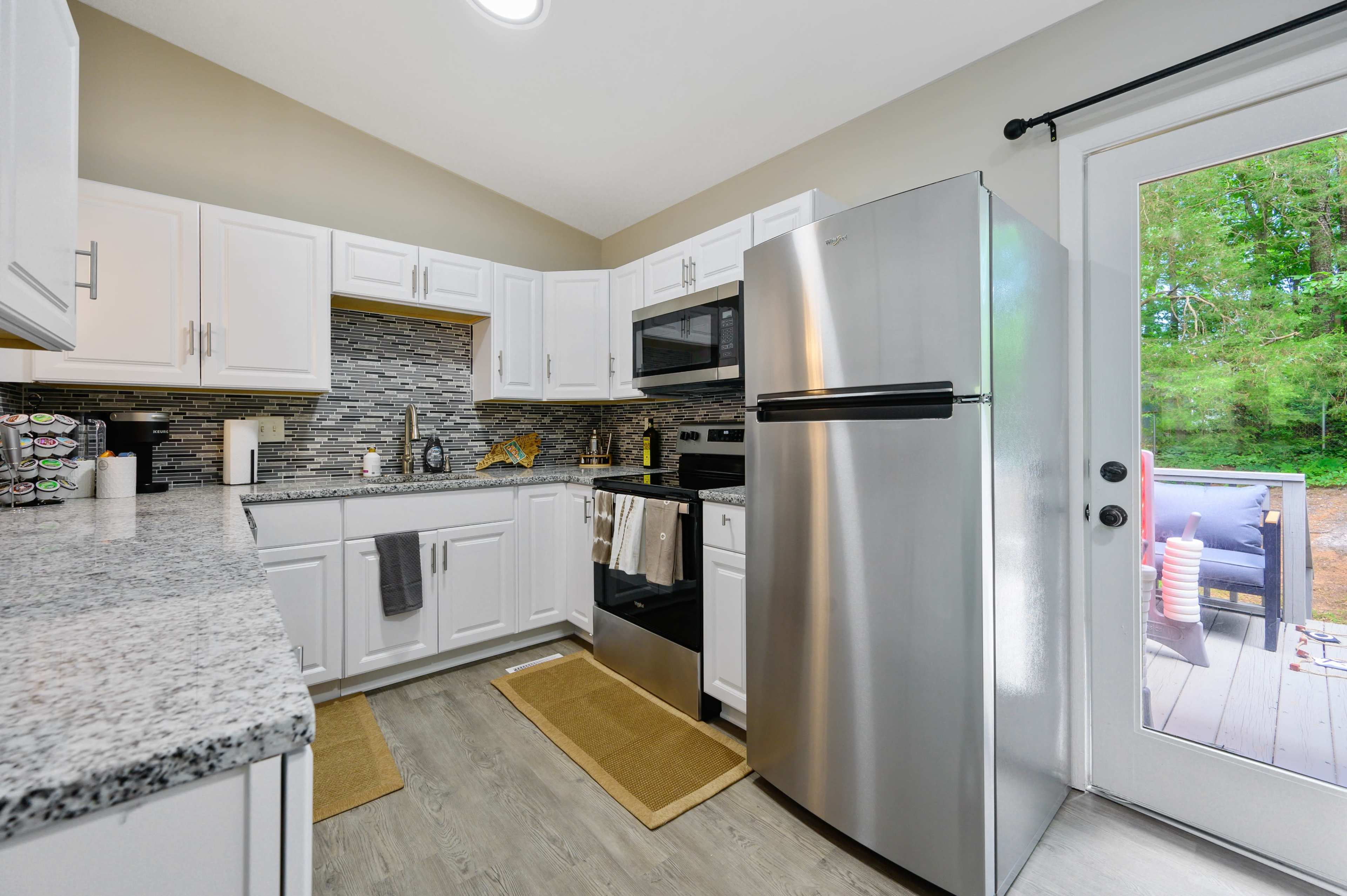 A modern kitchen featuring white cabinetry, a stainless steel refrigerator, and a door leading to a deck area.