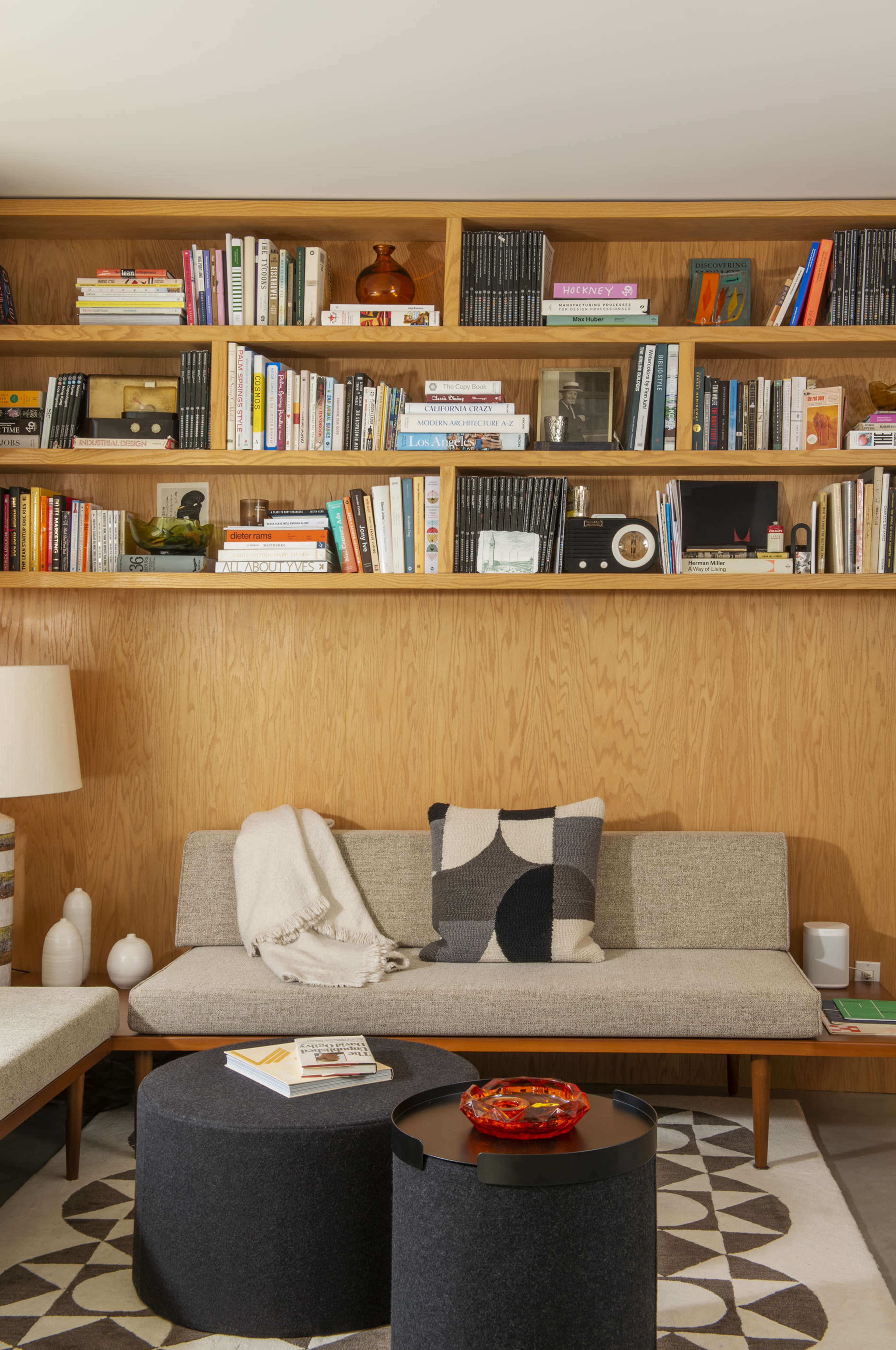 A stylish living room features a gray sofa with patterned cushions, a round black coffee table, and a wooden bookshelf filled with various books and decor items.