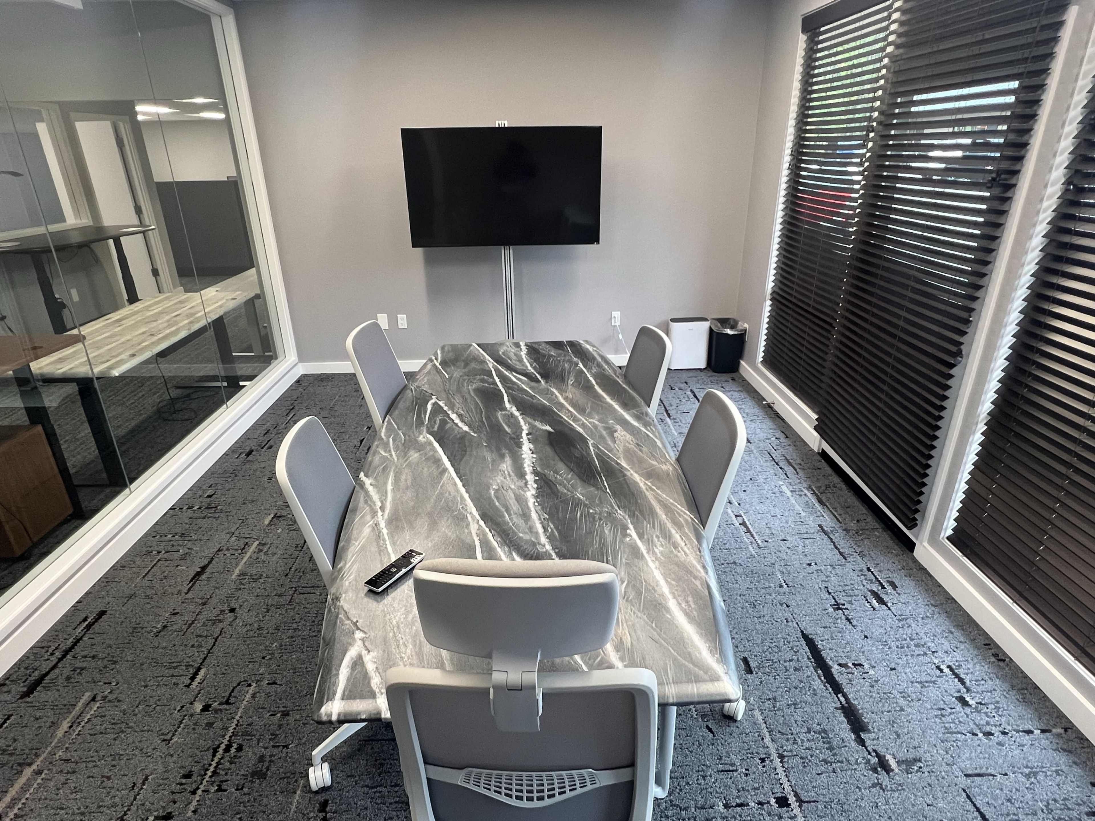A sleek conference room features a large marble table surrounded by six chairs and a wall-mounted television.