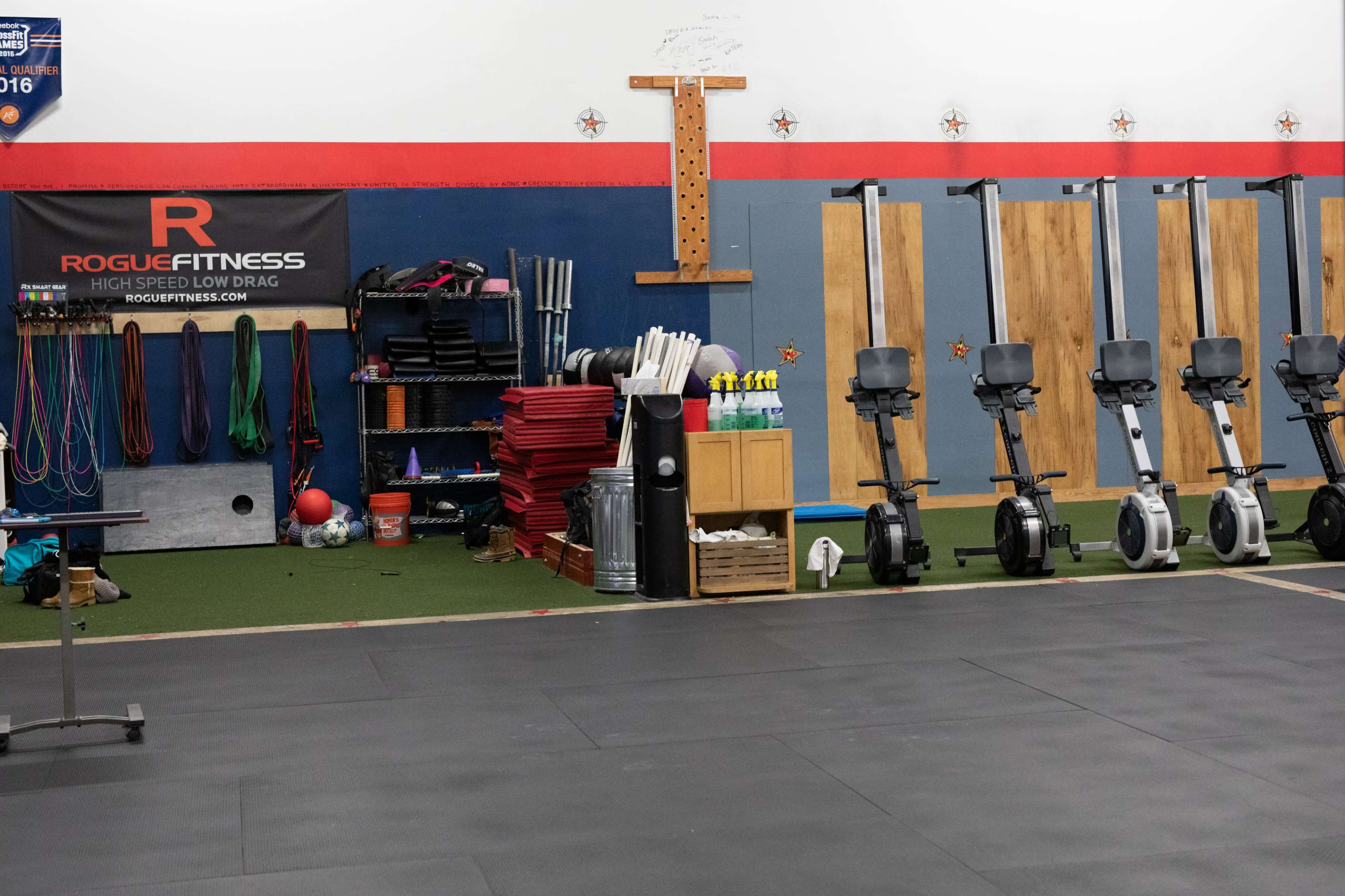 A gym space featuring exercise equipment, including rowing machines and various fitness accessories organized along a wall.