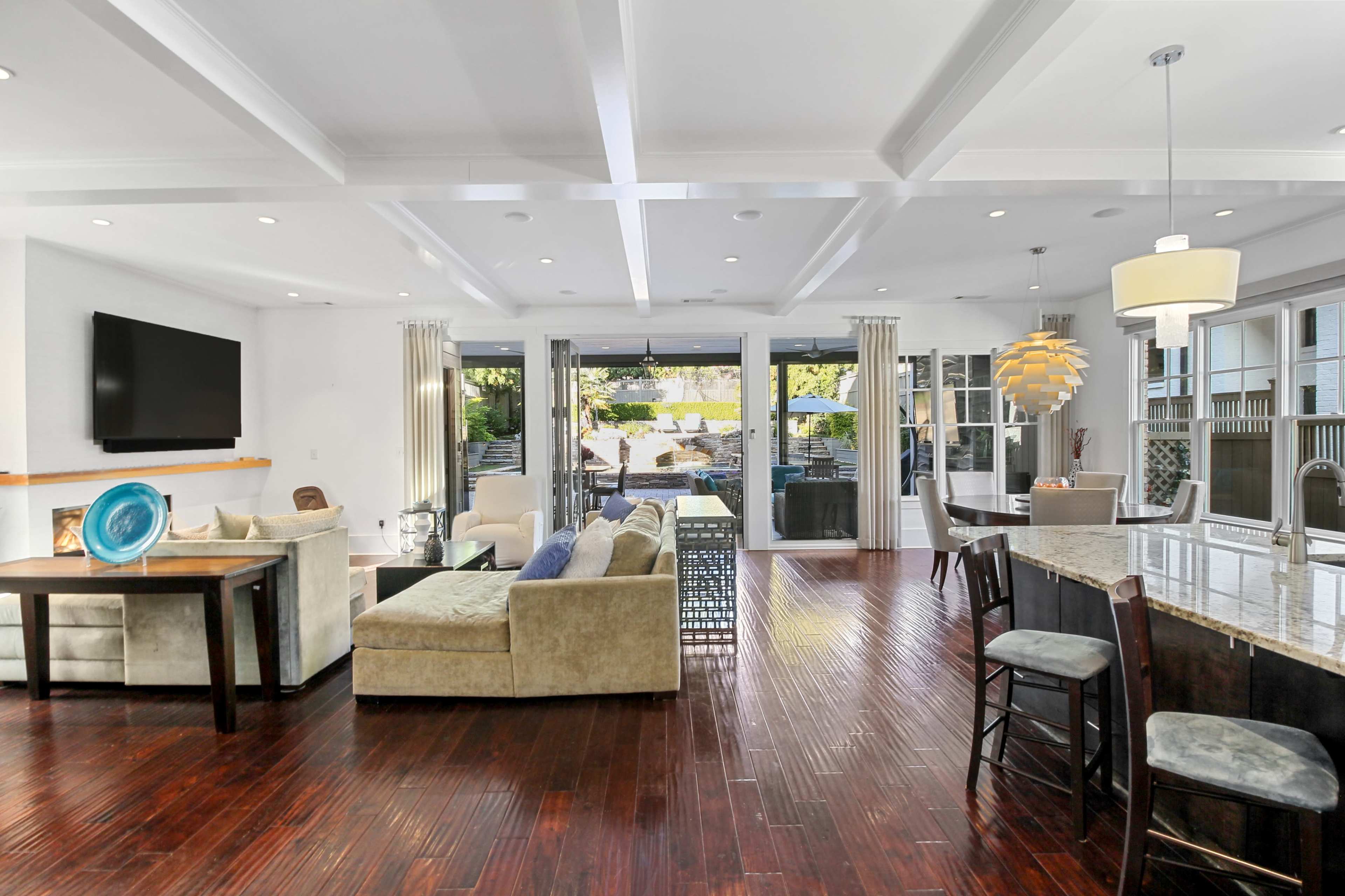 The open-concept living area features a modern sectional sofa, a dining table, and large windows overlooking a patio and outdoor space.
