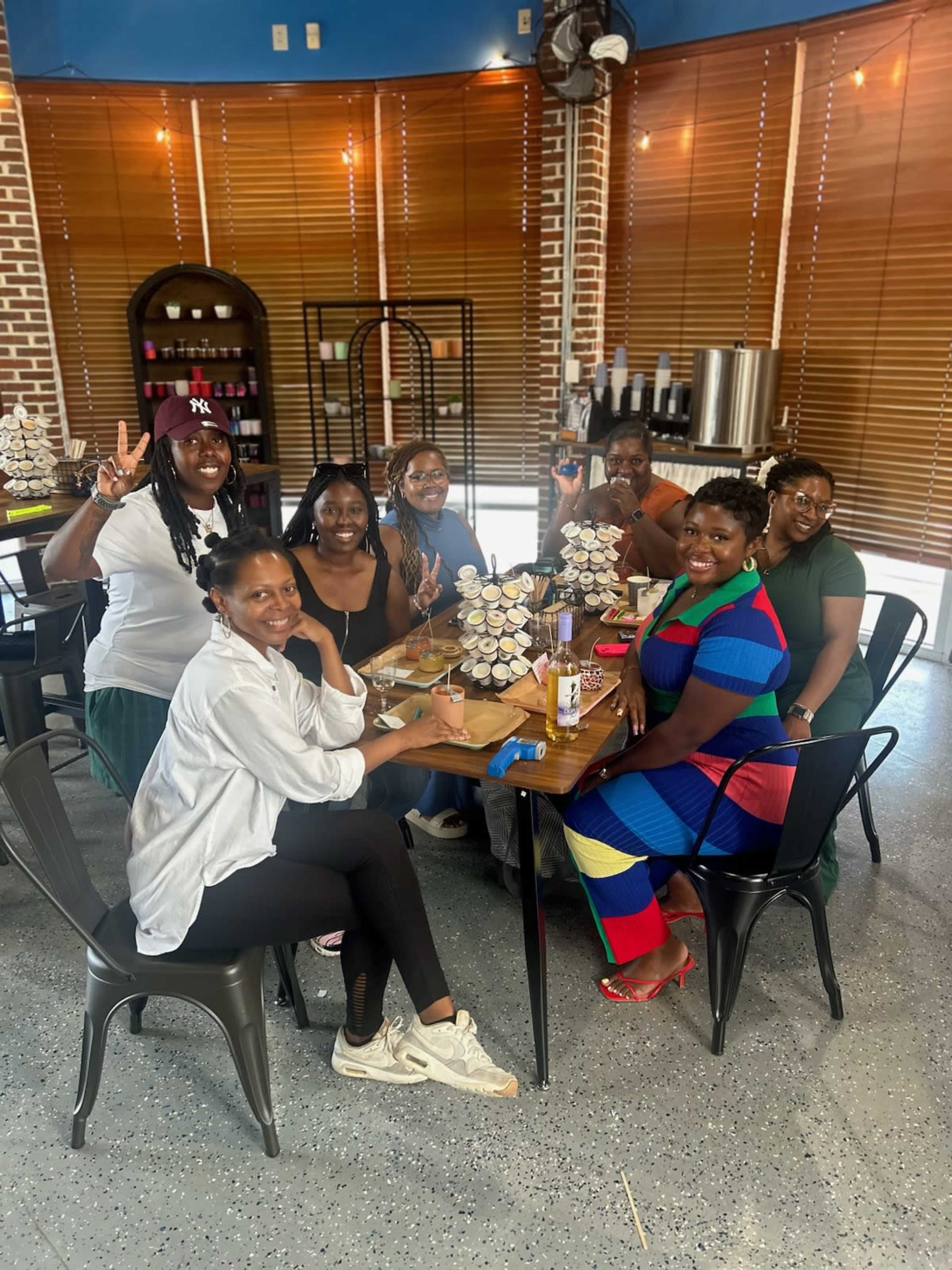 A group of seven women sits around a table in a brightly lit café, smiling and posing for the camera.