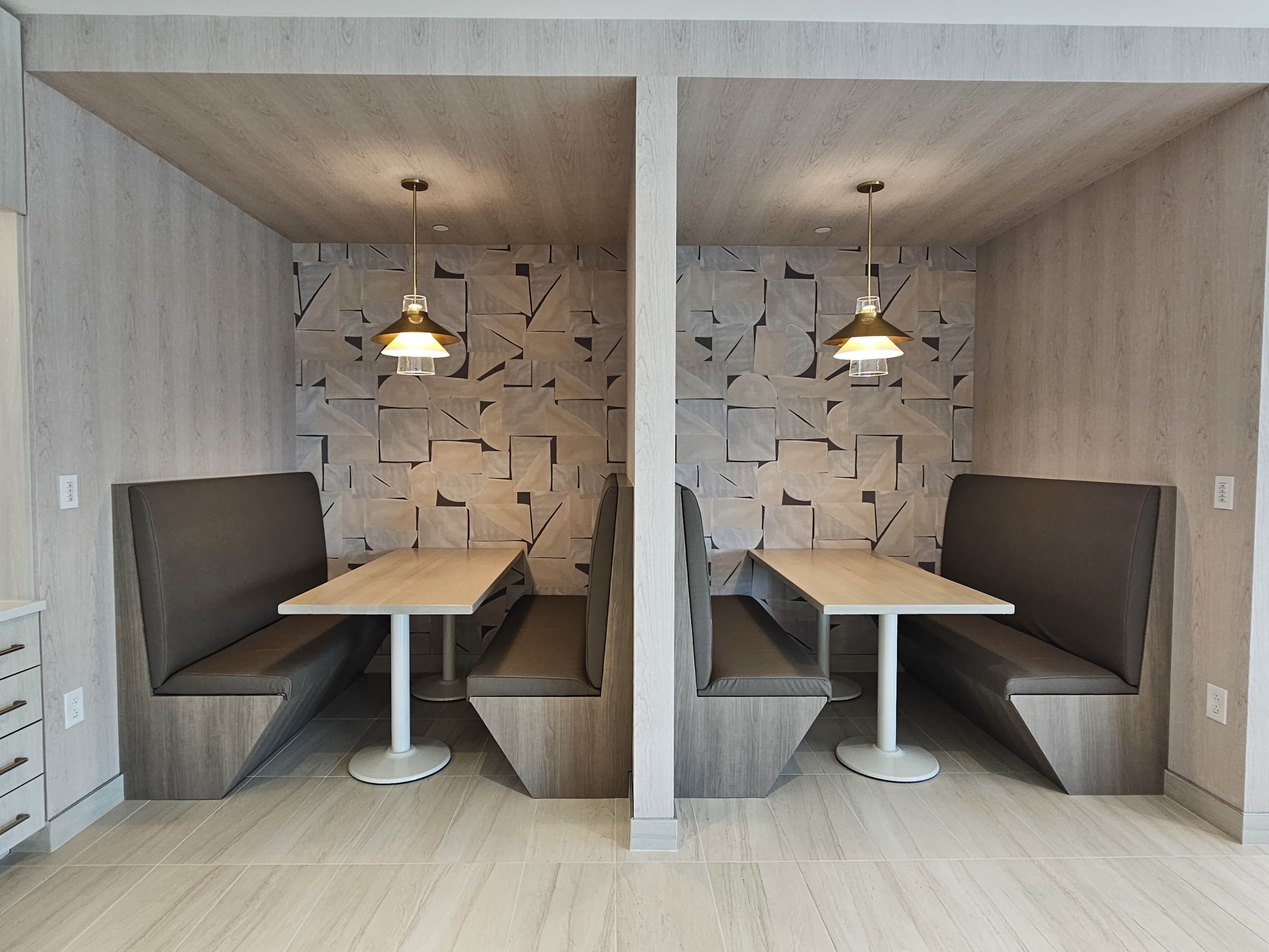Two semi-enclosed booths with wooden walls and modern pendant lights, each containing a table and seating.