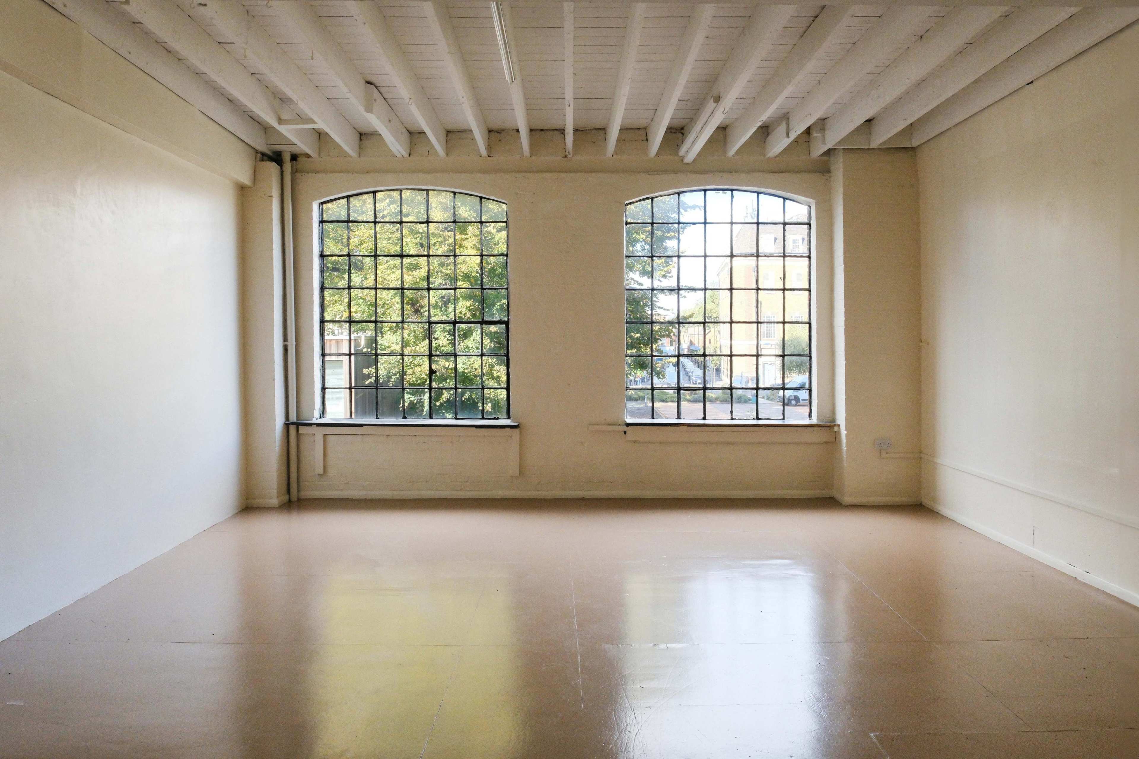 A bare room with two large arched windows and polished floors, illuminated by natural light.