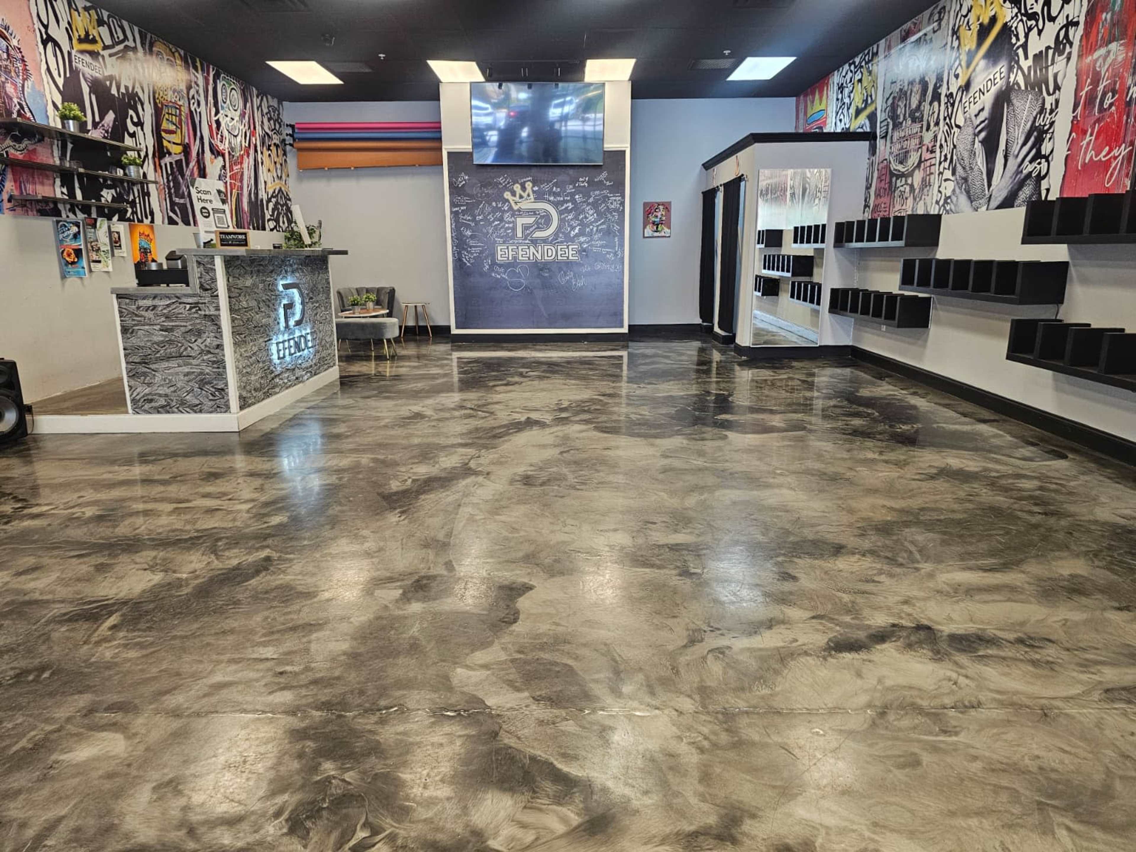 The interior of a modern retail space features polished concrete flooring, a reception desk with a backlit logo, and colorful graffiti-style wall art.