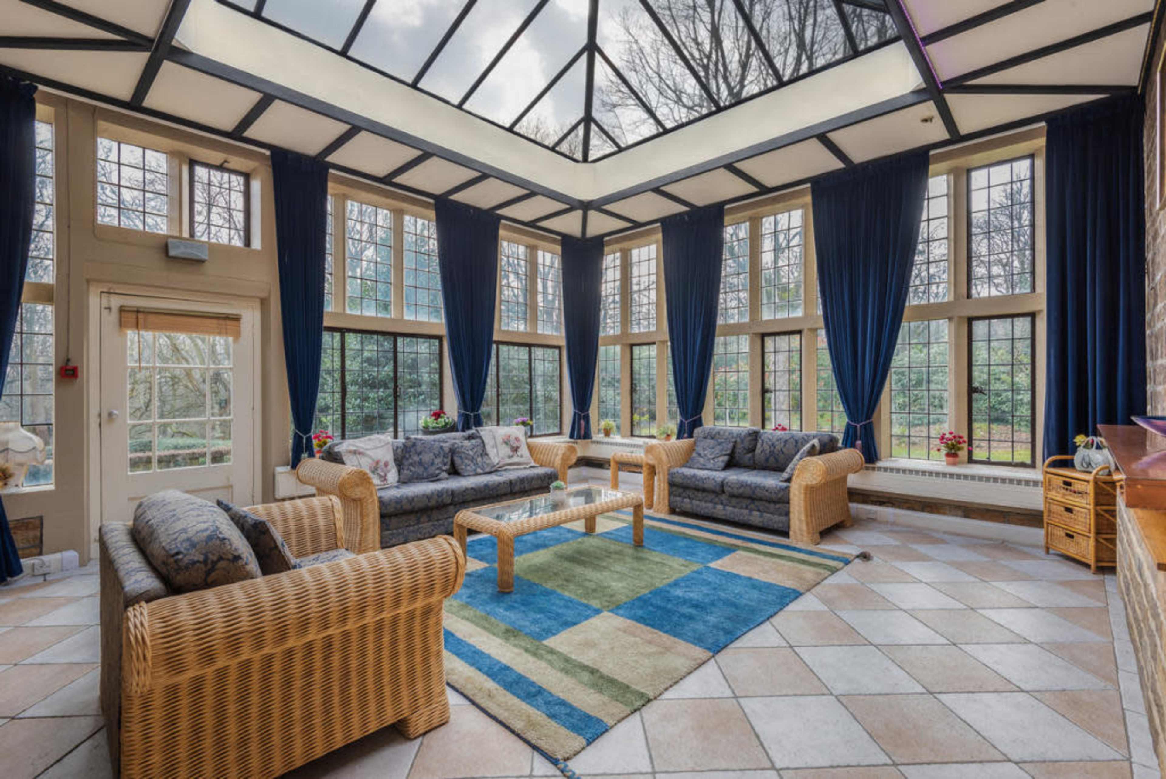 A sunroom filled with wicker furniture, large windows, and a tiled floor, illuminated by natural light.
