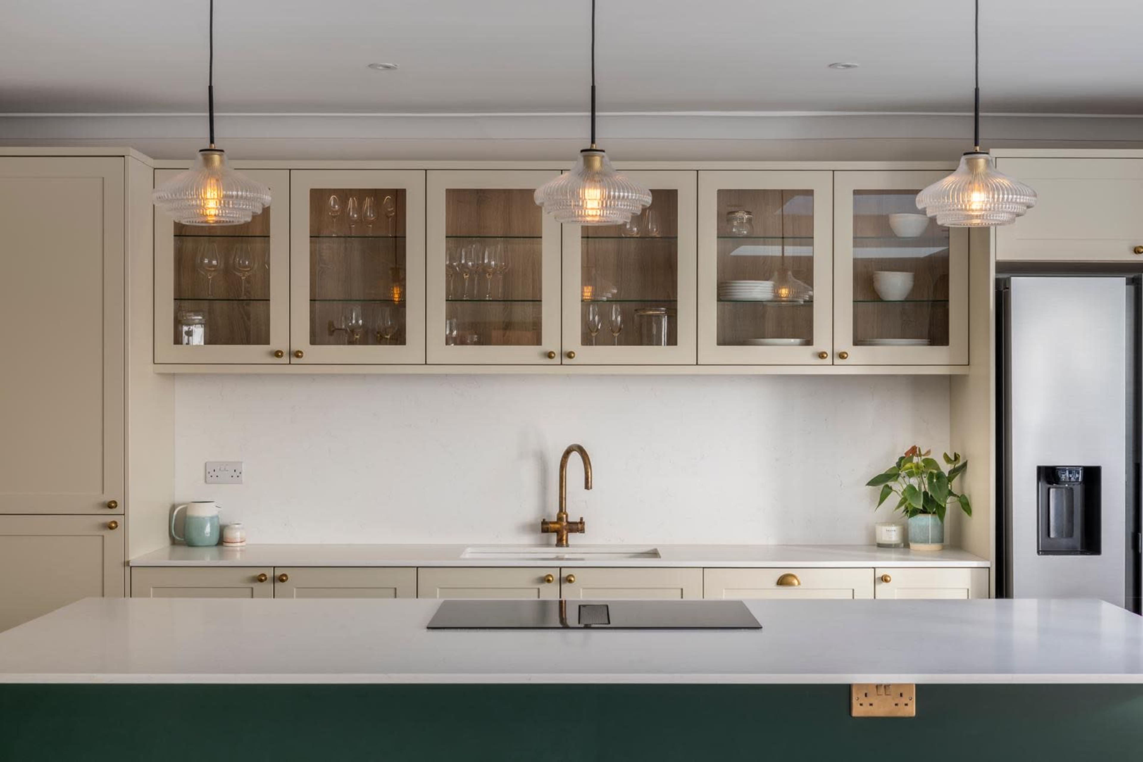 The image shows a modern kitchen featuring light-colored cabinetry, a white countertop, and pendant lighting above a central island.