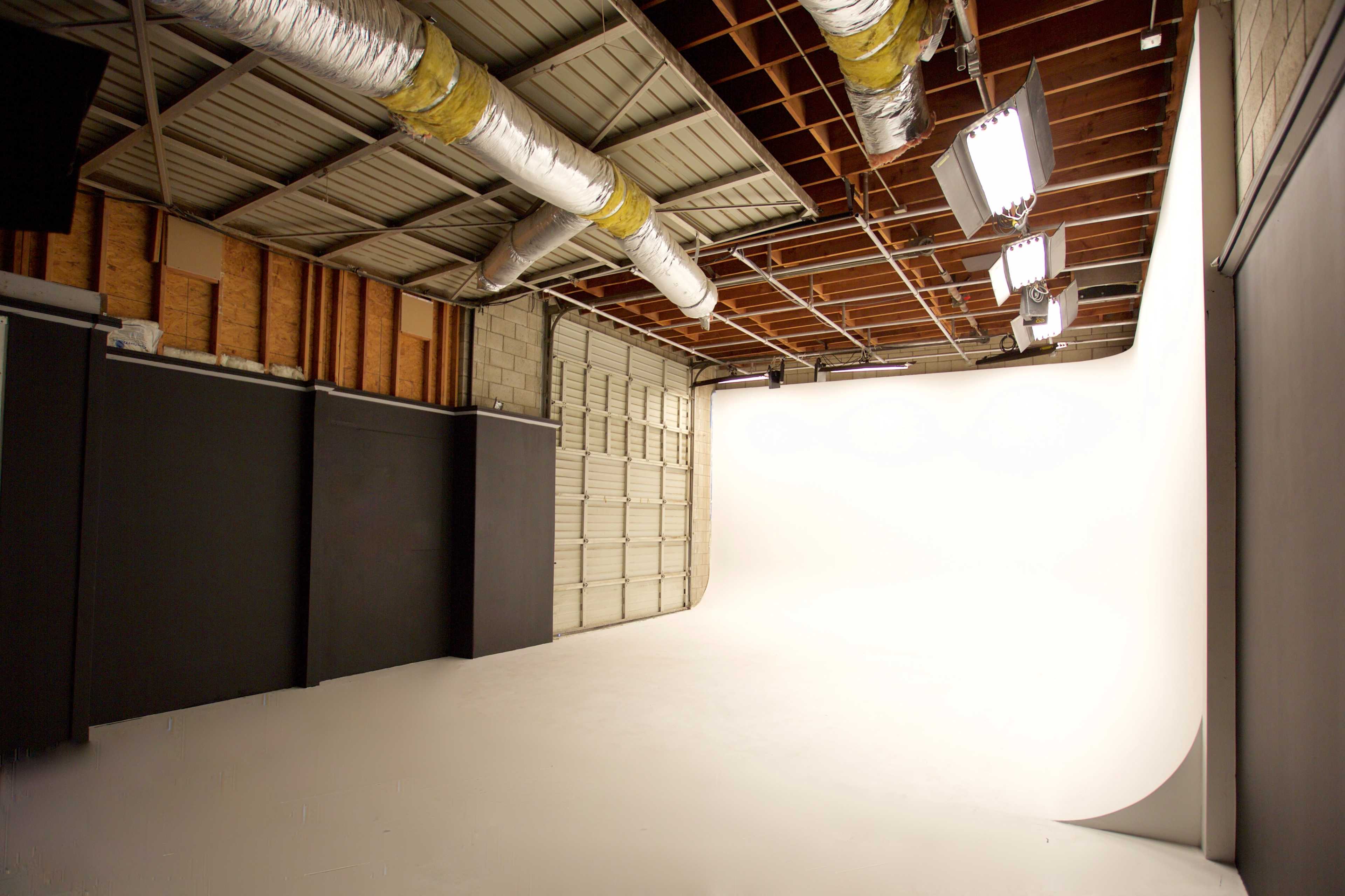 A spacious photography studio with a seamless white backdrop and various lighting fixtures overhead.