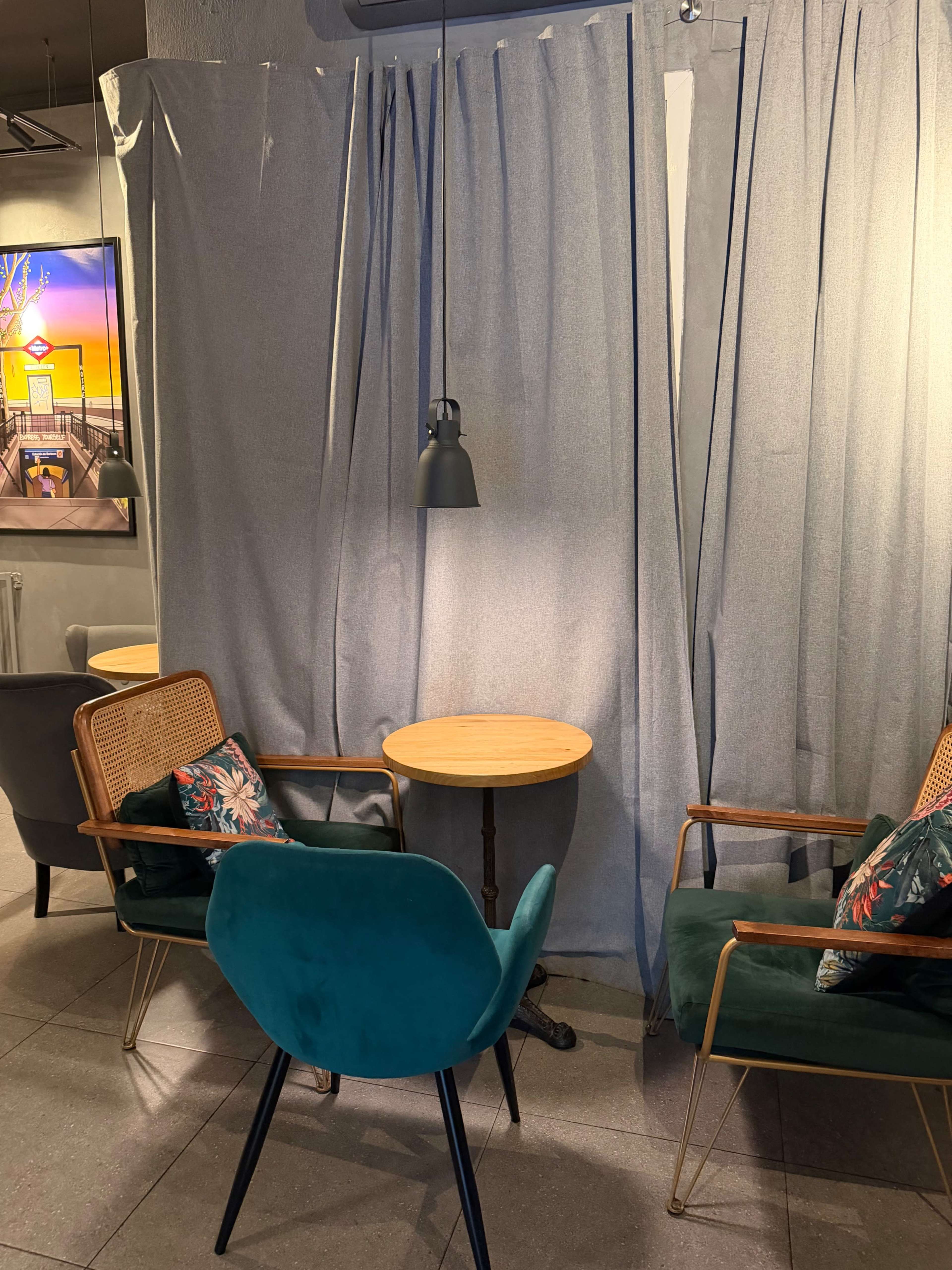 A small seating area features two chairs, a round table, and gray curtains, set against a backdrop of an artistic wall display.