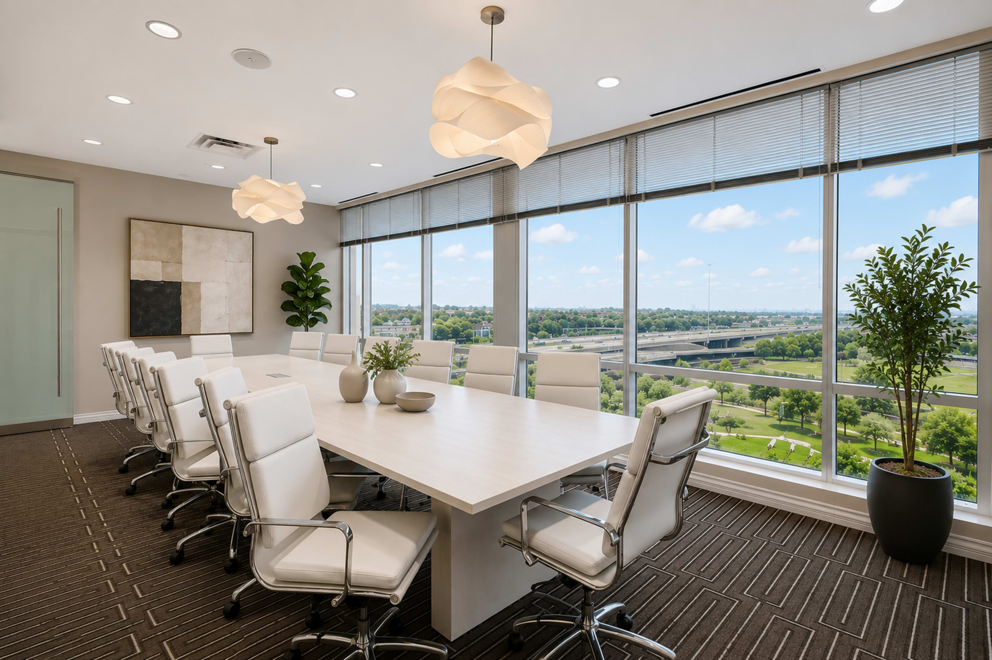 A modern conference room features a long white table surrounded by sleek white chairs, with large windows offering a view of green landscapes and a bridge outside.