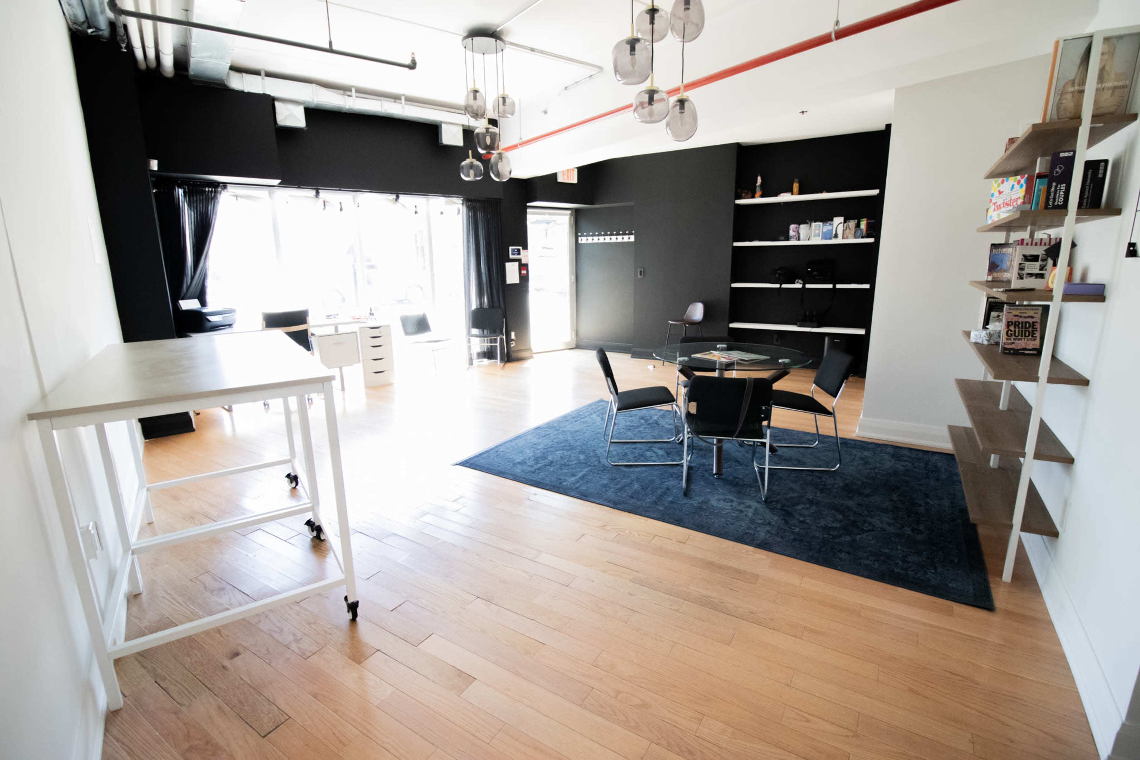 The image shows a modern office space featuring a circular glass table surrounded by chairs, hardwood flooring, and large windows allowing natural light.