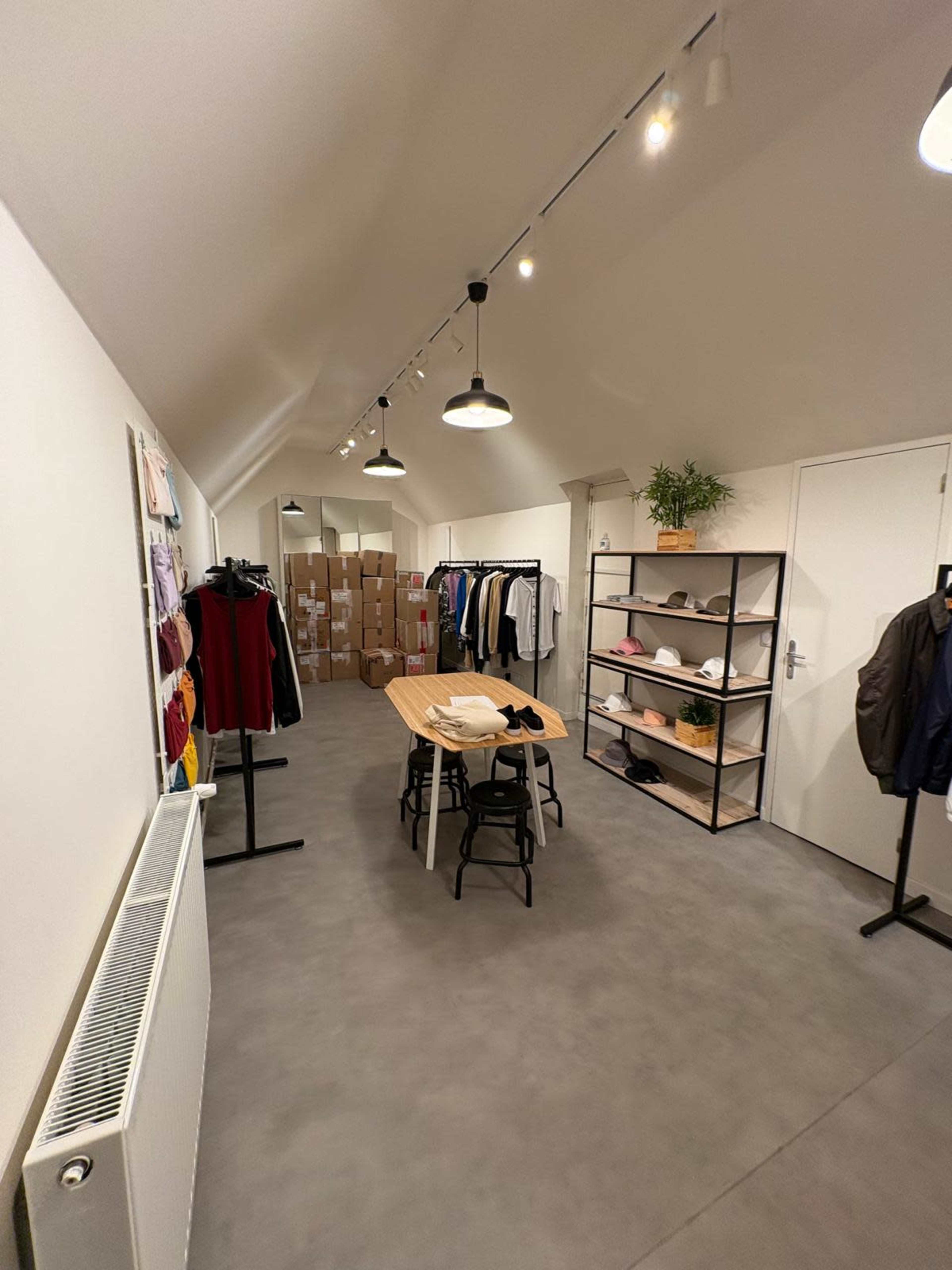 The image shows a tidy room with a long wooden table, clothing racks, and several boxes stacked against one wall.