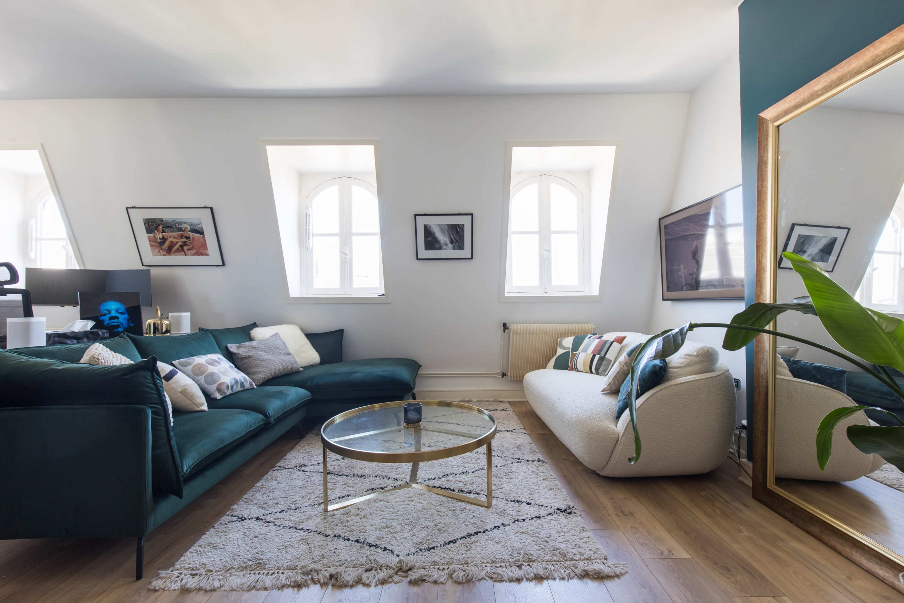 A modern living room with a green sofa, a light-colored couch, a glass coffee table on a textured rug, and several framed pictures on the walls.