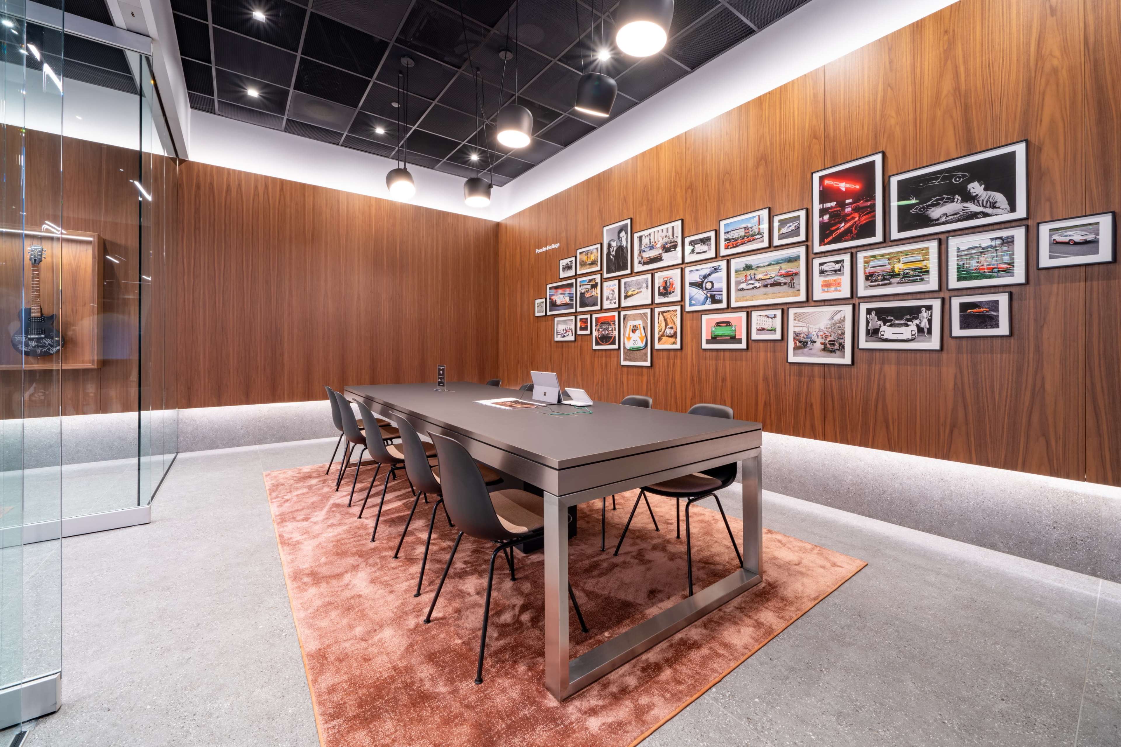 A modern conference room features a long table surrounded by chairs, with framed art on the walls and a glass partition.