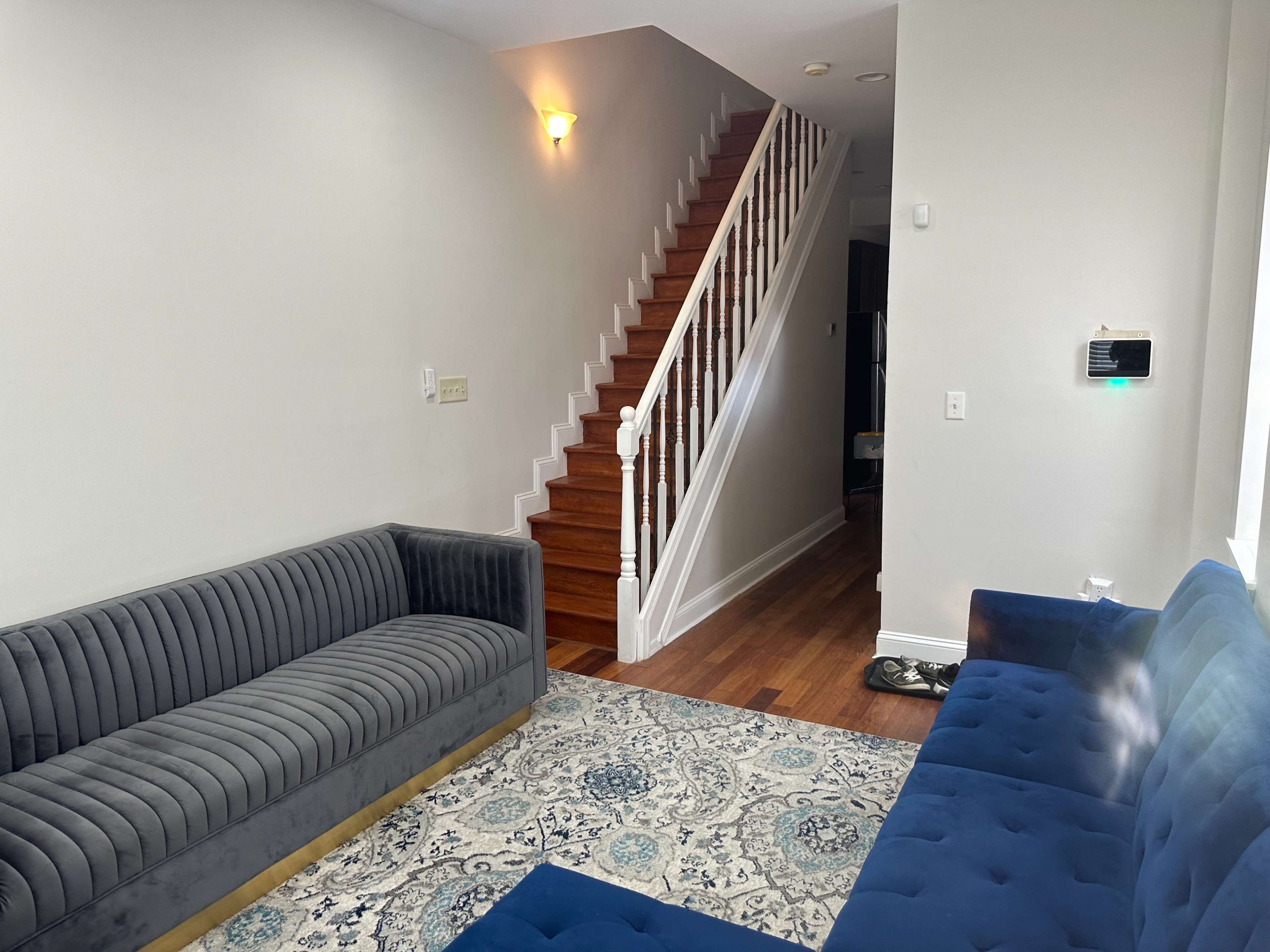 A living room with a blue velvet sofa, a gray striped couch, and a staircase leading to an upper level.