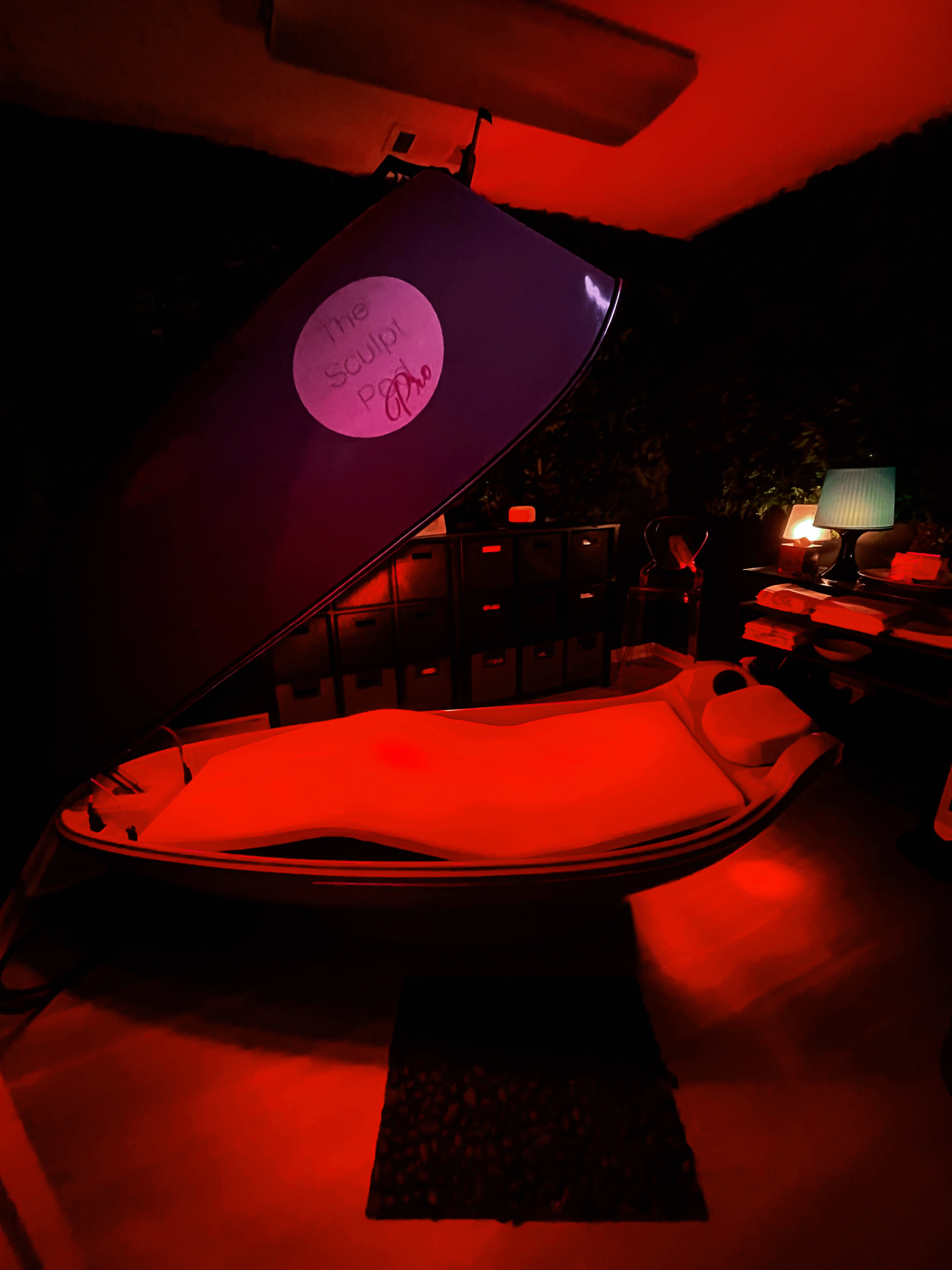 A floatation therapy pod is open in a dimly lit room, surrounded by dark walls and ambient lighting.