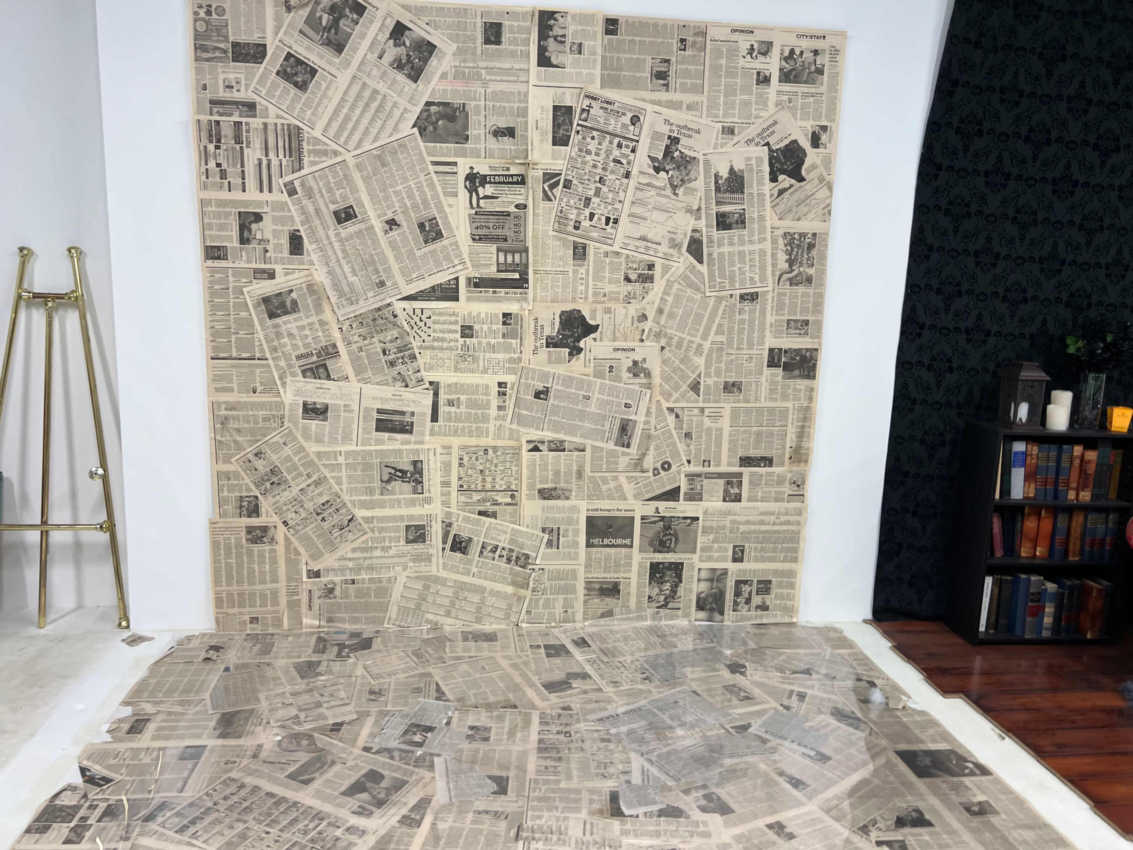 The image shows a wall and floor covered with various pieces of old newspaper, creating a vintage aesthetic.