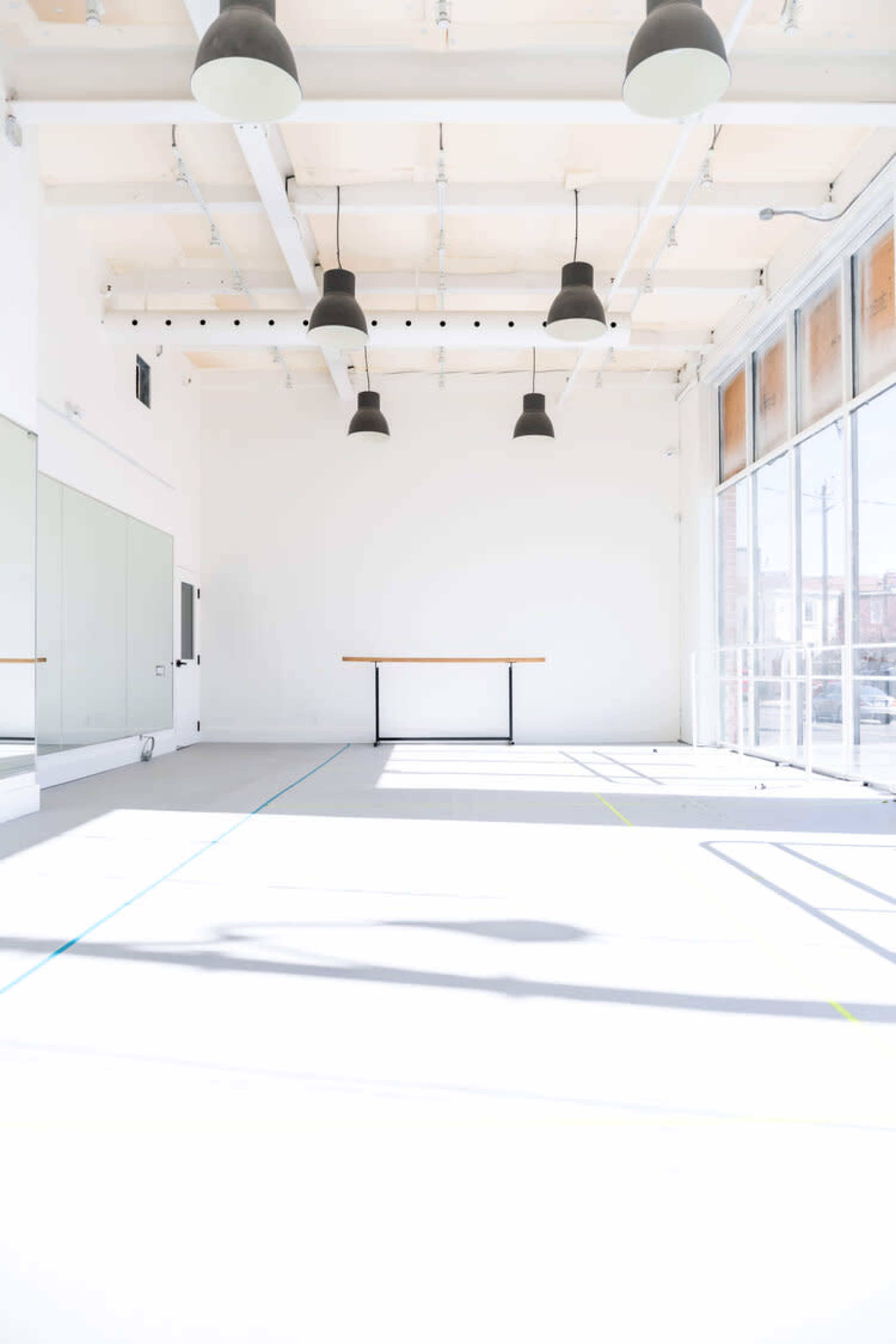 An empty, bright studio space with large windows, high ceilings, and a central table.