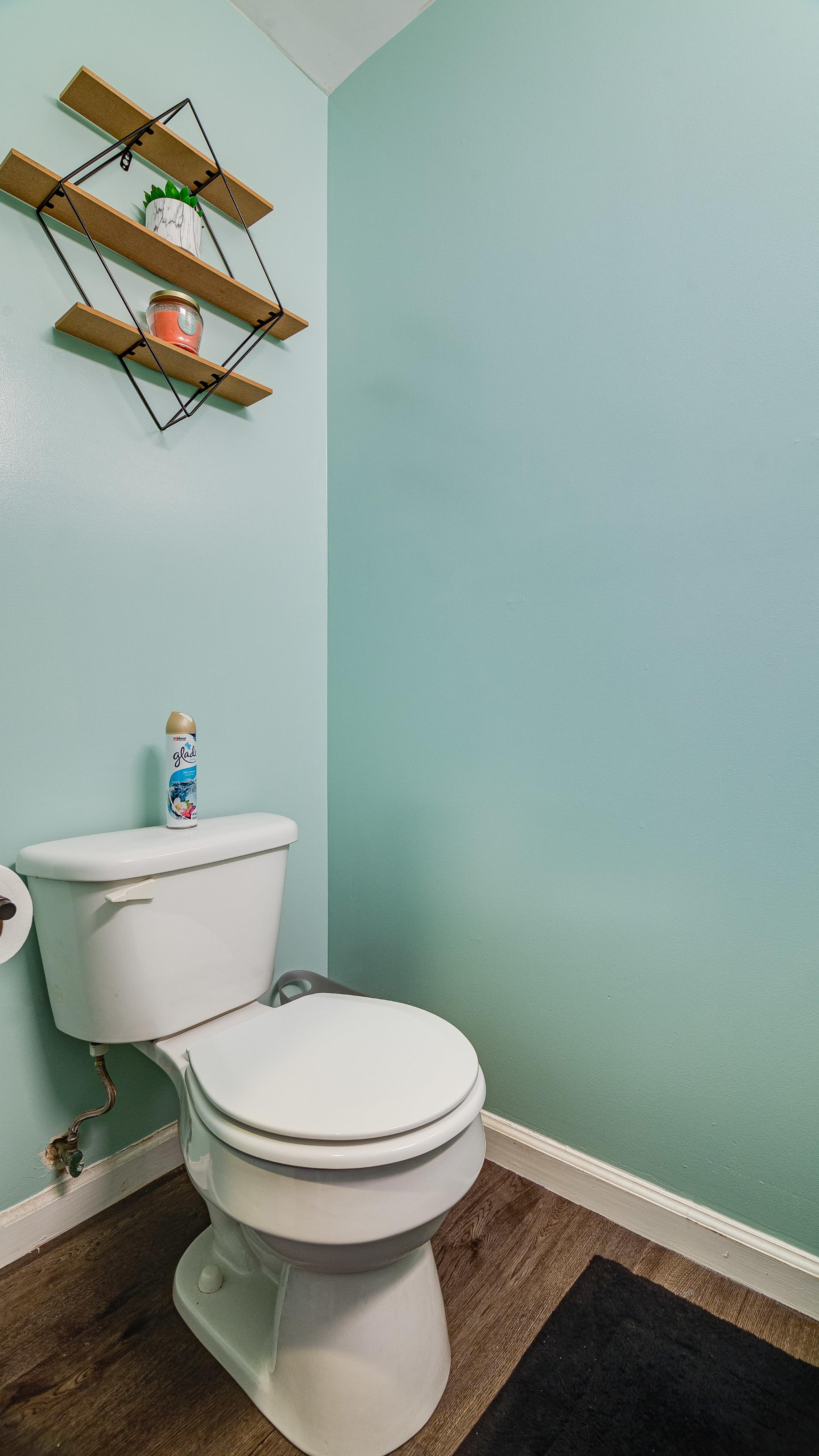 A clean bathroom with a toilet against a light blue wall and a black bath mat on the floor.