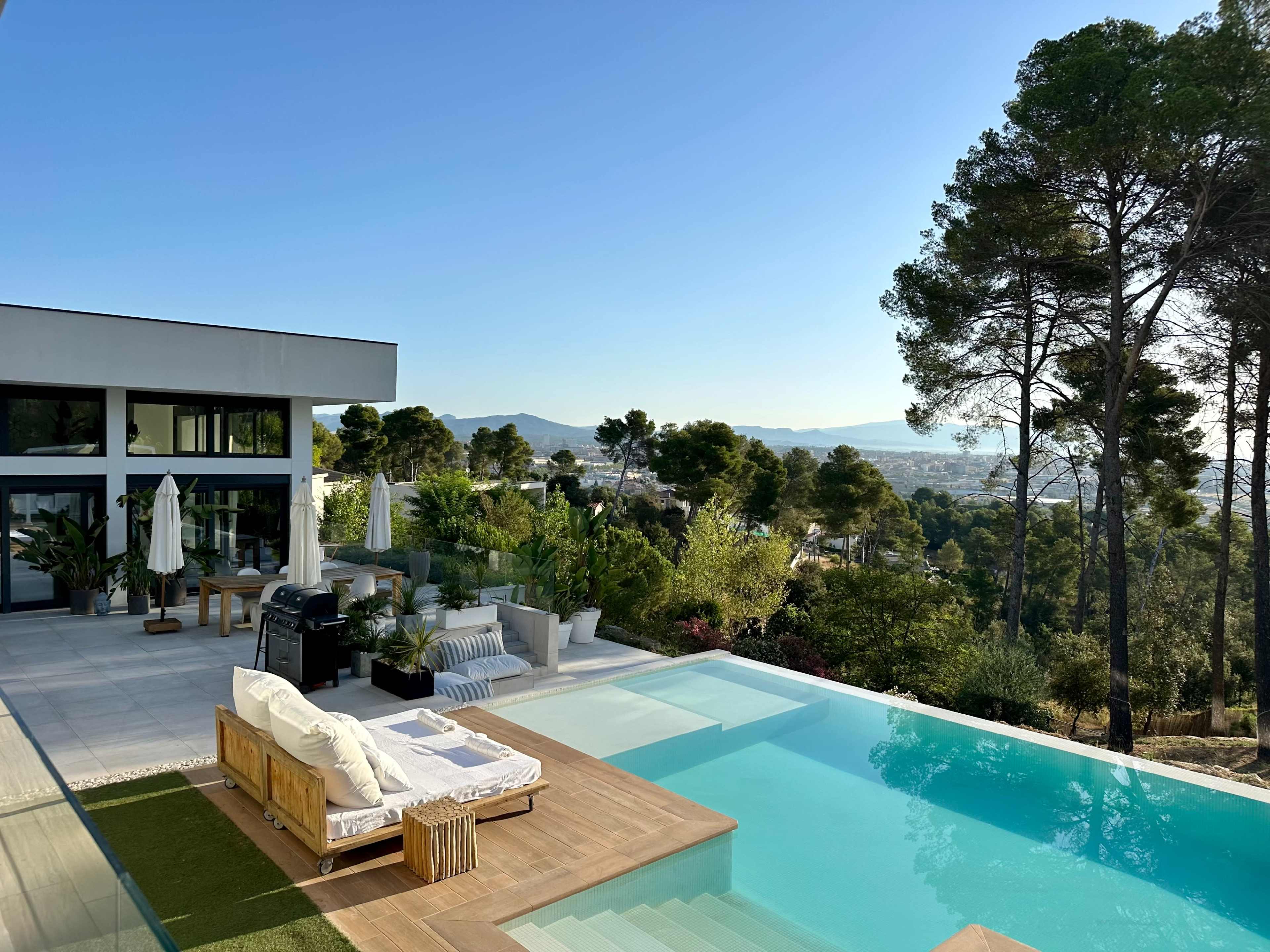 The image shows a modern villa with a swimming pool overlooking a scenic view of hills and trees.