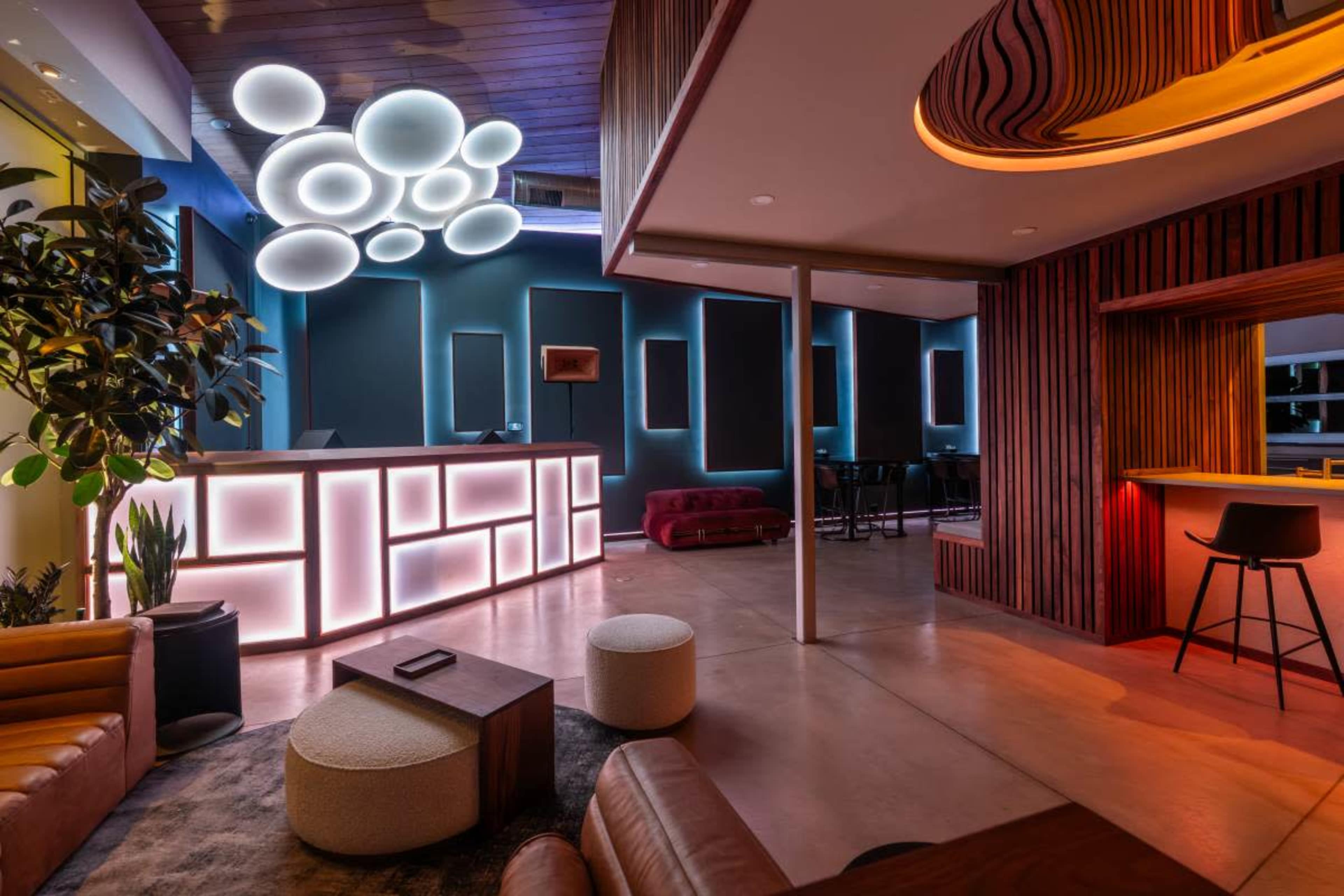 The image shows a modern lobby area featuring a unique illuminated reception desk, comfortable seating, and decorative lighting elements.