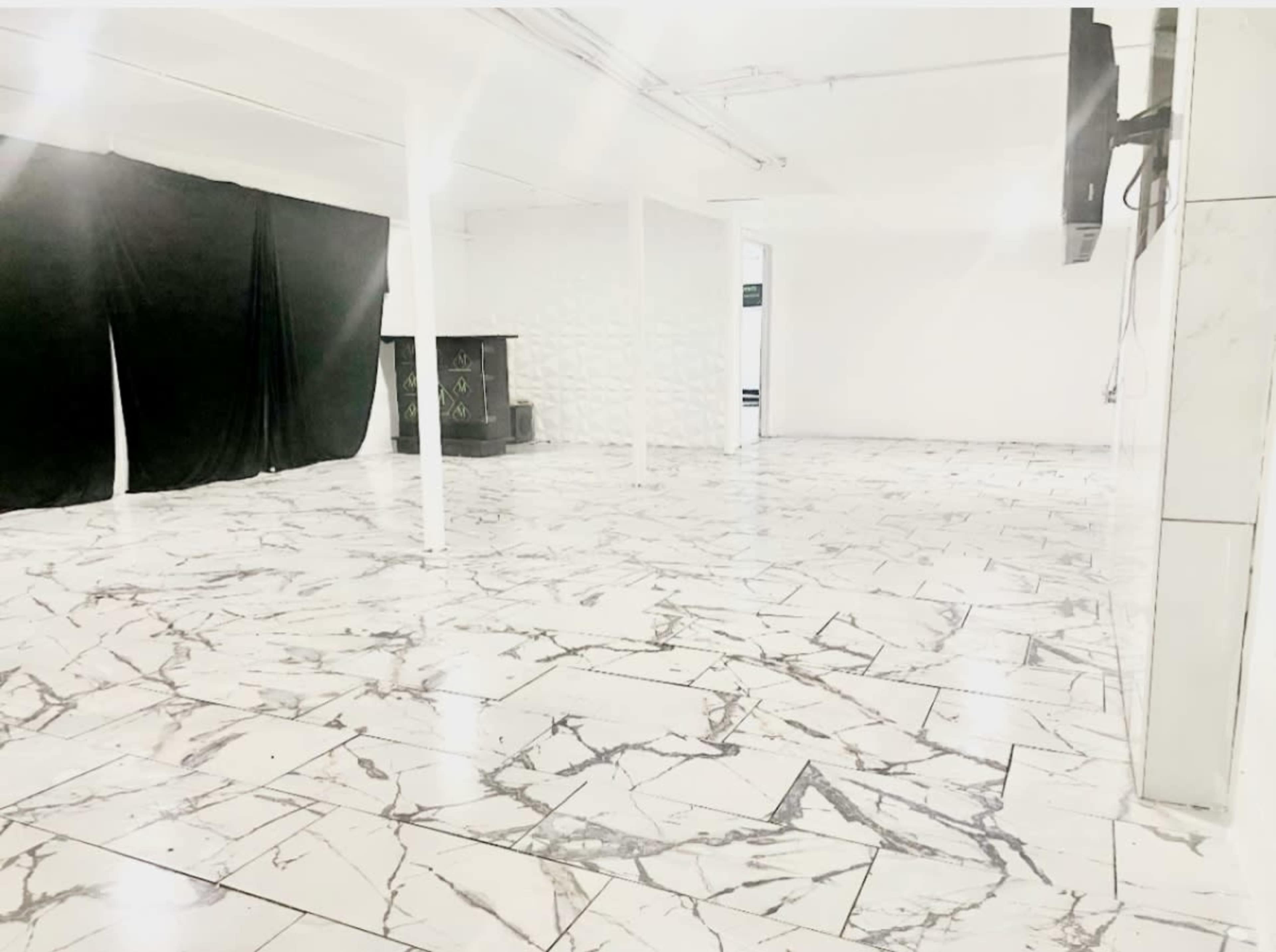 A large, empty room with white marble flooring, a black backdrop on one side, and a textured white wall opposite.