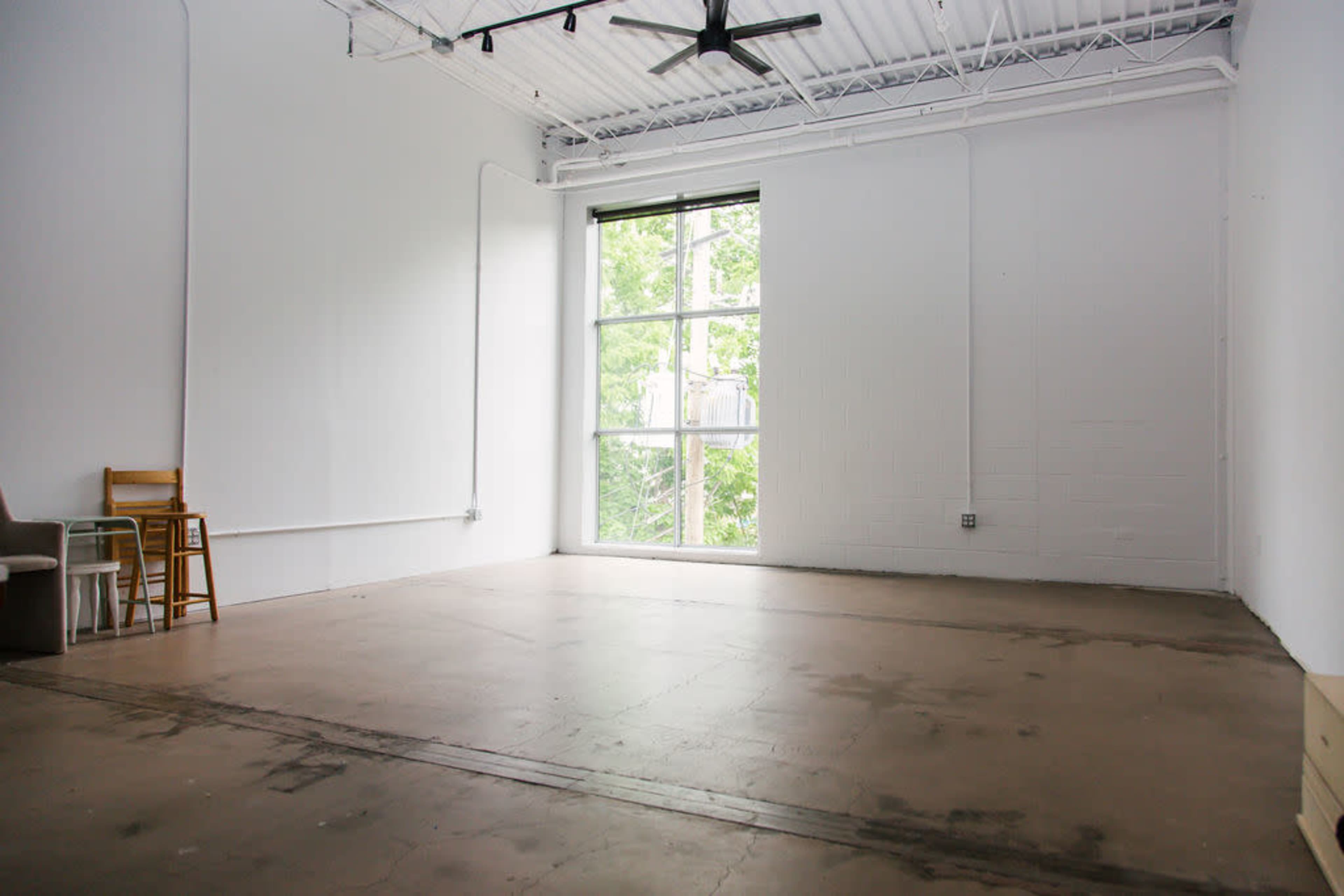 An empty room with smooth concrete flooring, a large window letting in natural light, and minimal furnishings.
