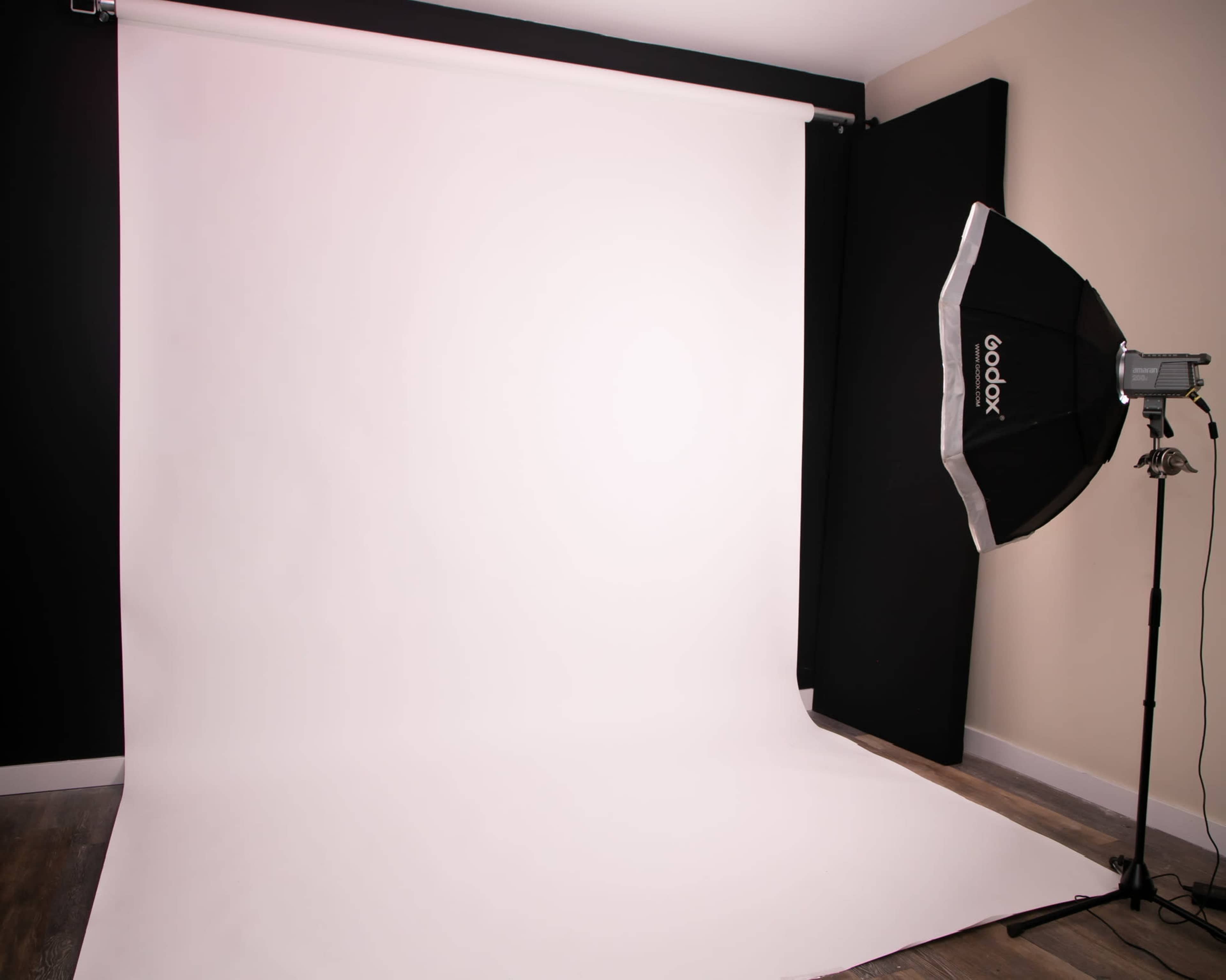 A photography studio with a large white backdrop and a lighting setup on the side.