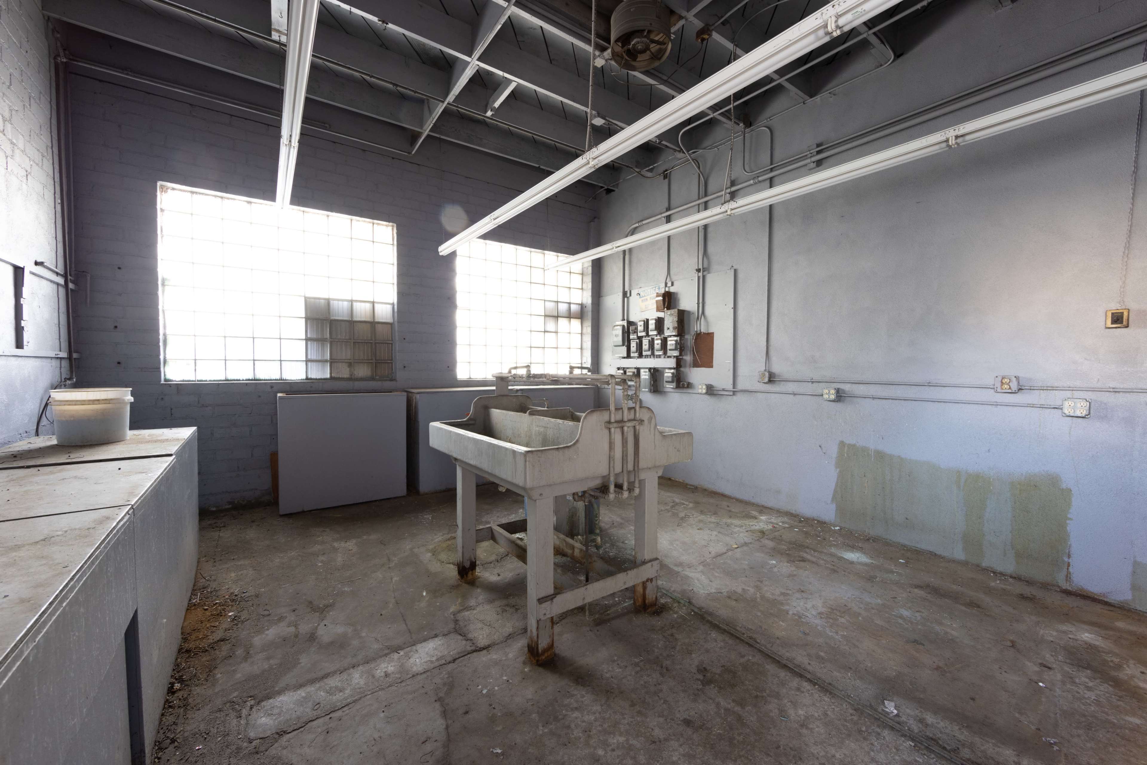 An empty industrial room with gray walls, two windows, and a central sink or worktable.