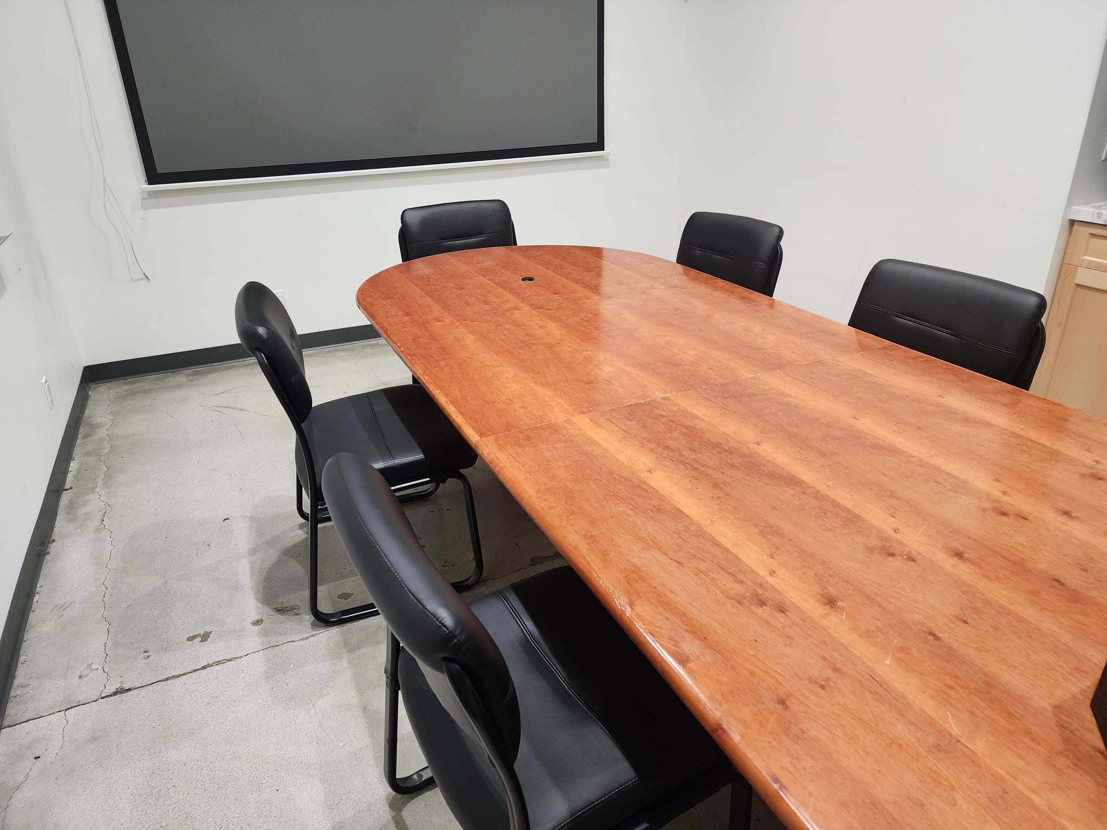 A large wooden conference table surrounded by six black chairs in a minimalist meeting room.