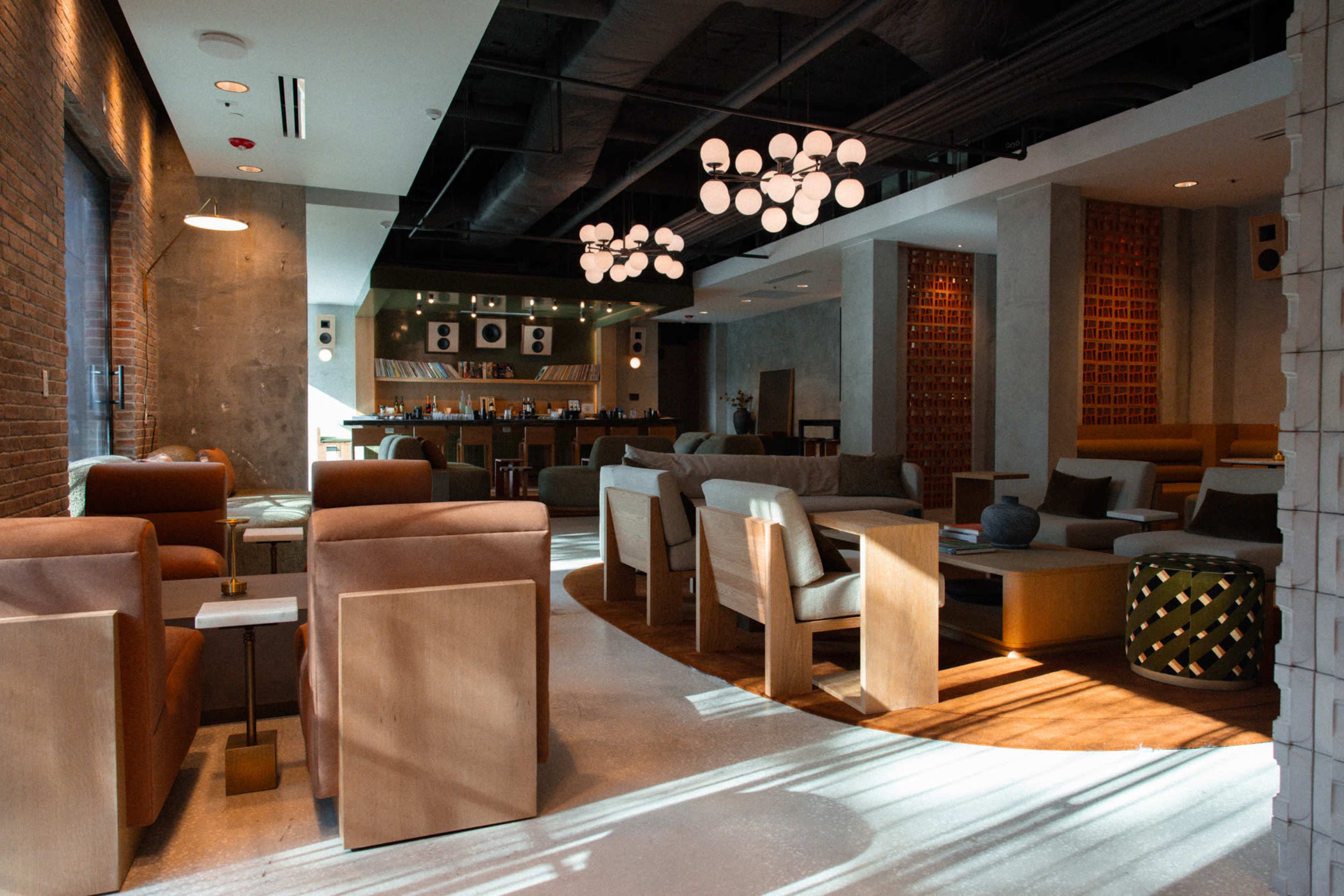 The image shows a modern lounge area with brown leather chairs, wooden furniture, and a bar in the background, illuminated by pendant lights.