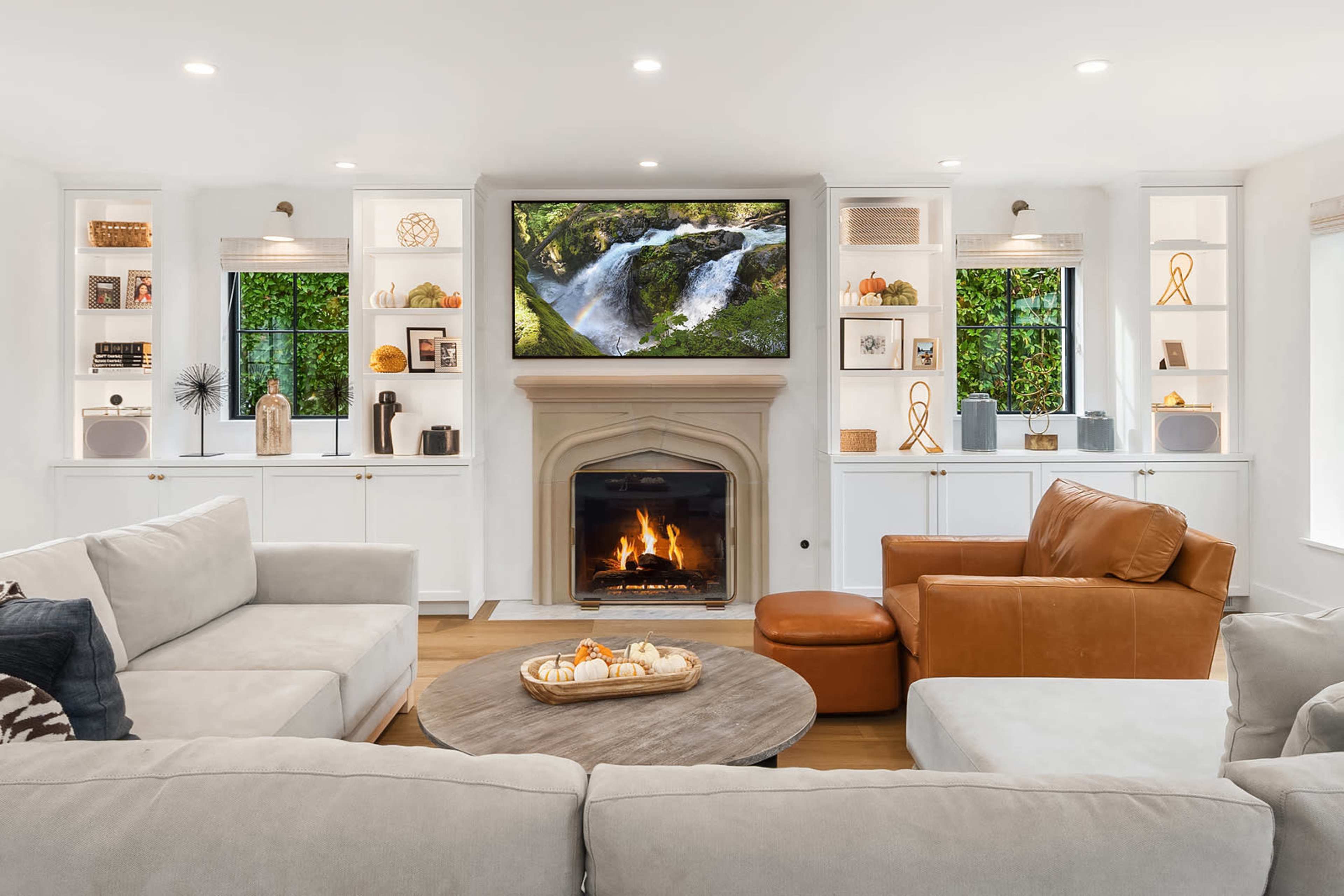 A cozy living room features a fireplace, a large TV mounted above it, and built-in shelves with decorative items.