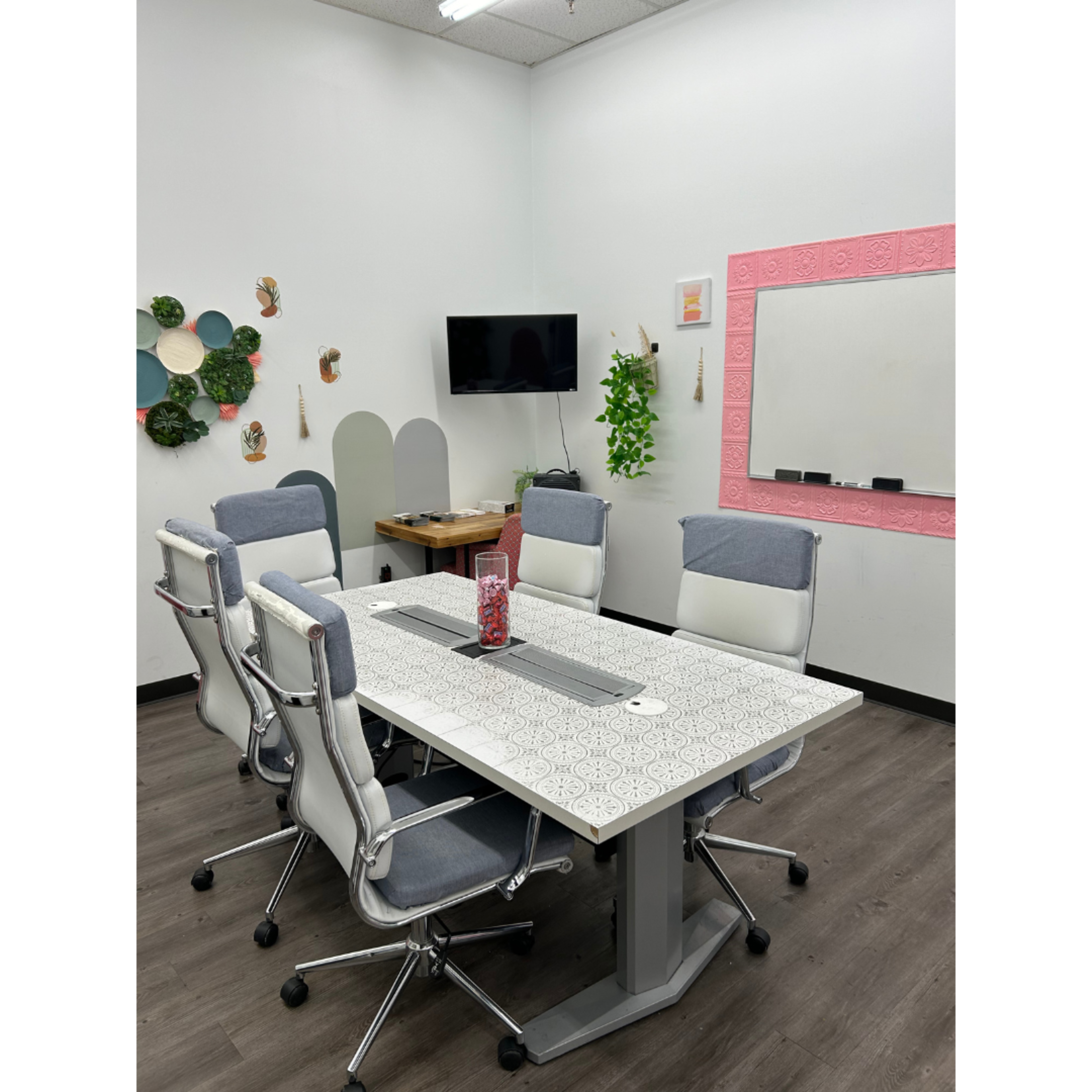 The image shows a modern conference room with a large table surrounded by six chairs, a wall-mounted TV, and decorative wall elements.