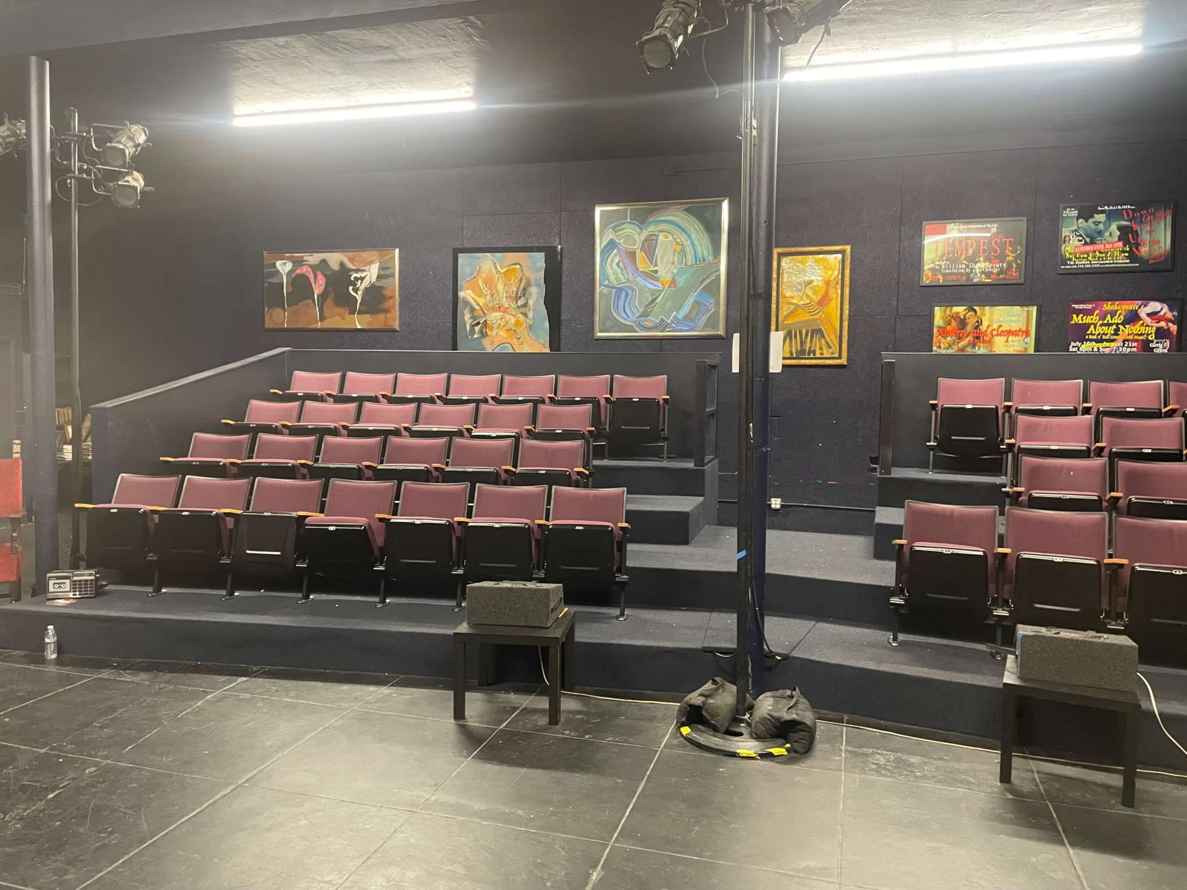 A theater stage with rows of maroon seats, colorful paintings on the walls, and stage lighting overhead.