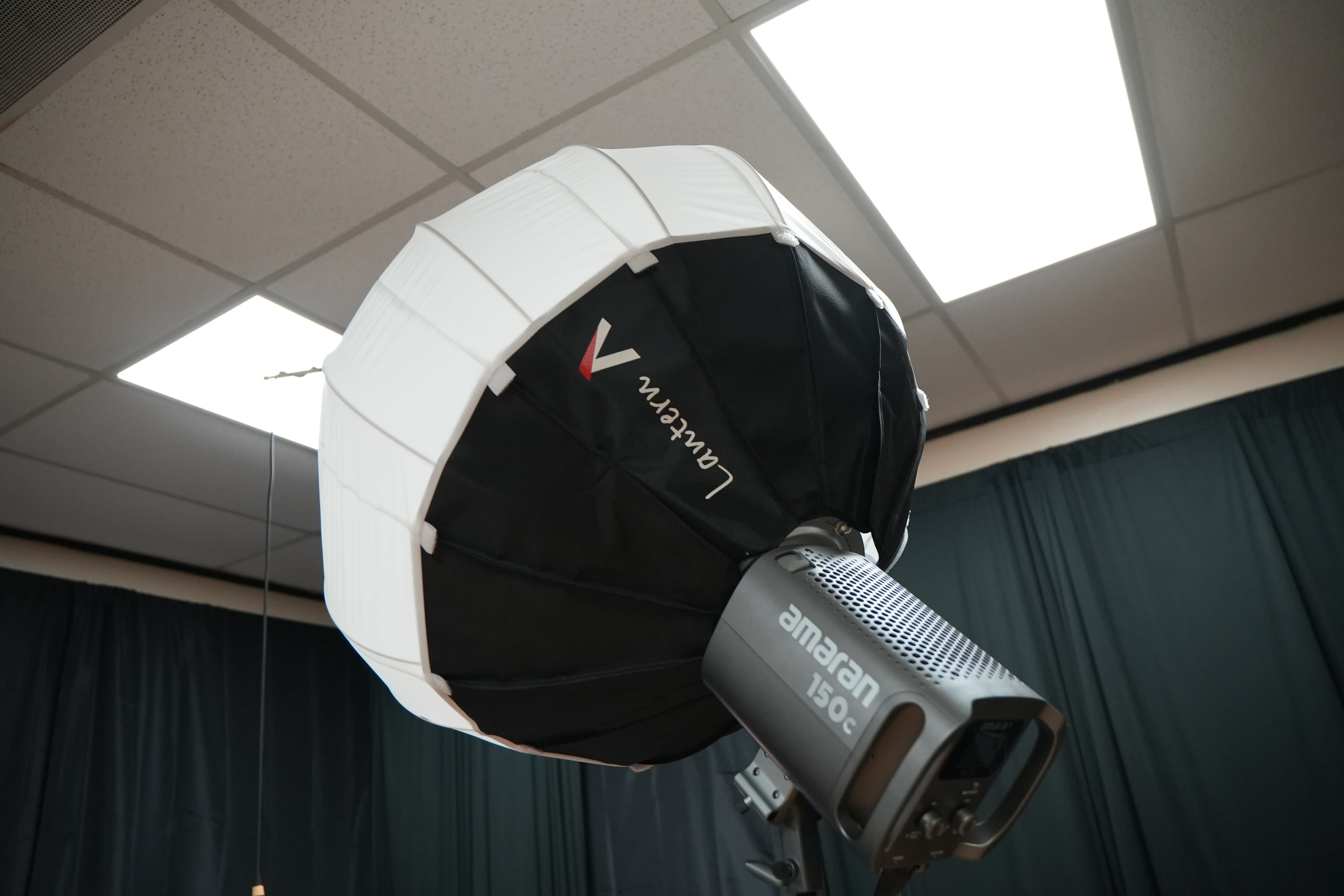 The image shows a large, white collapsible softbox attached to a flash unit in a photography studio.